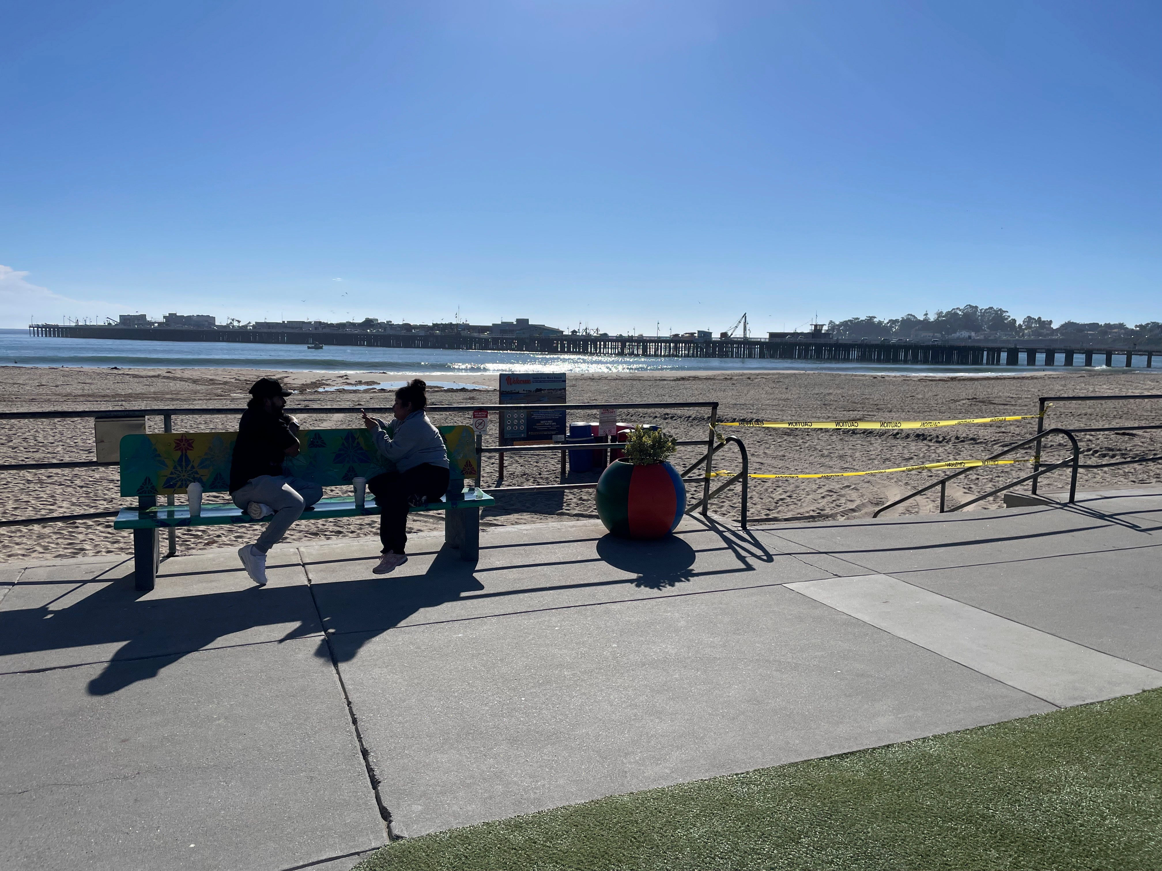 People sit on a bench along the beach in Santa Cruz, California, after authorities cleared the main beach. They taped off entrances