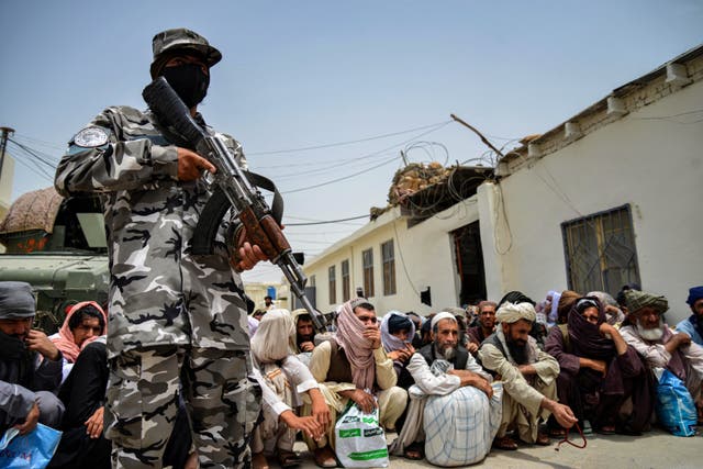 <p>An armed Taliban guard stands over prisoners in Kandahar </p>