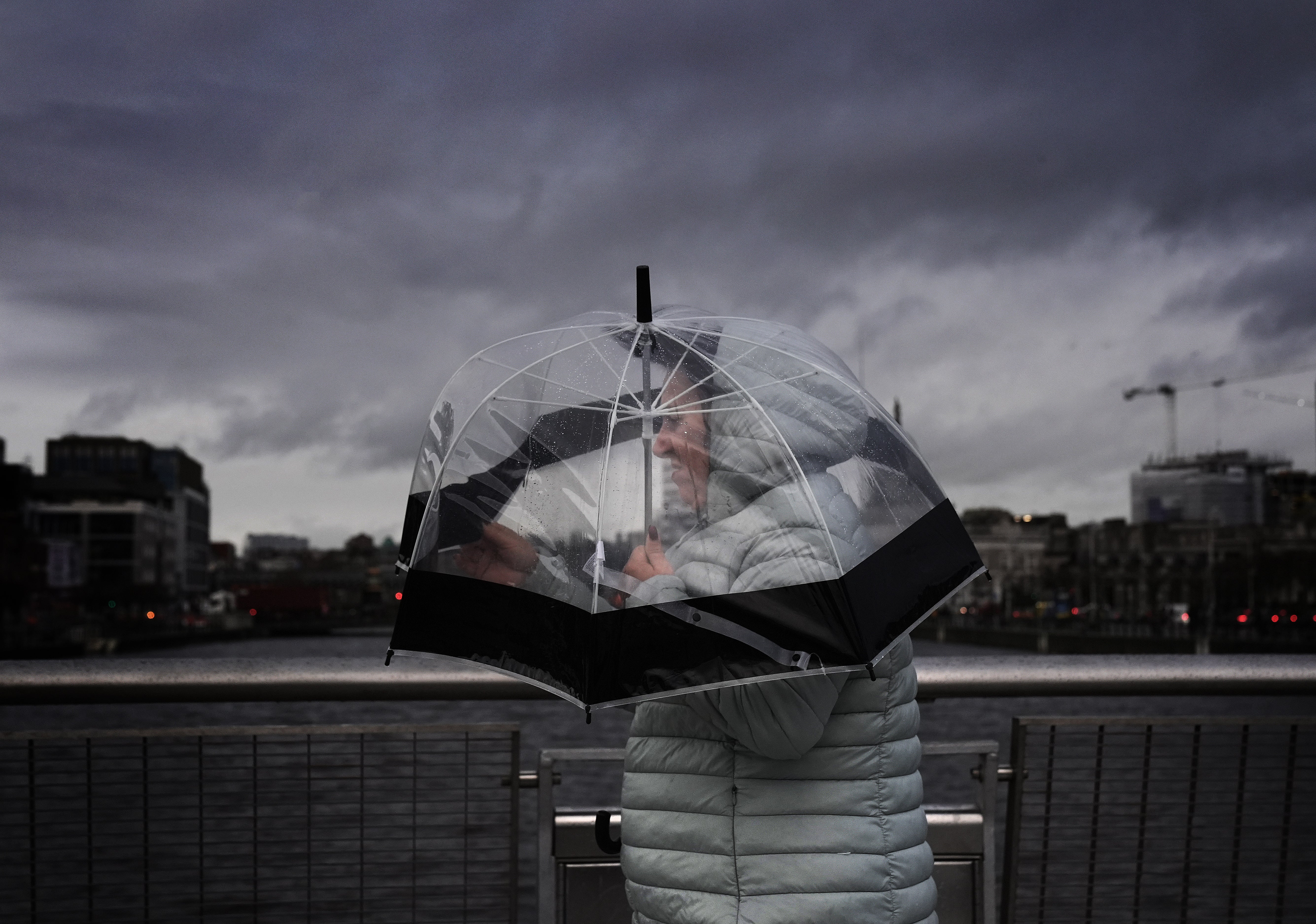 A person takes shelter under an umbrella as they cross the Sean O’Casey Bridge in Dublin city centre ahead of Storm Darragh