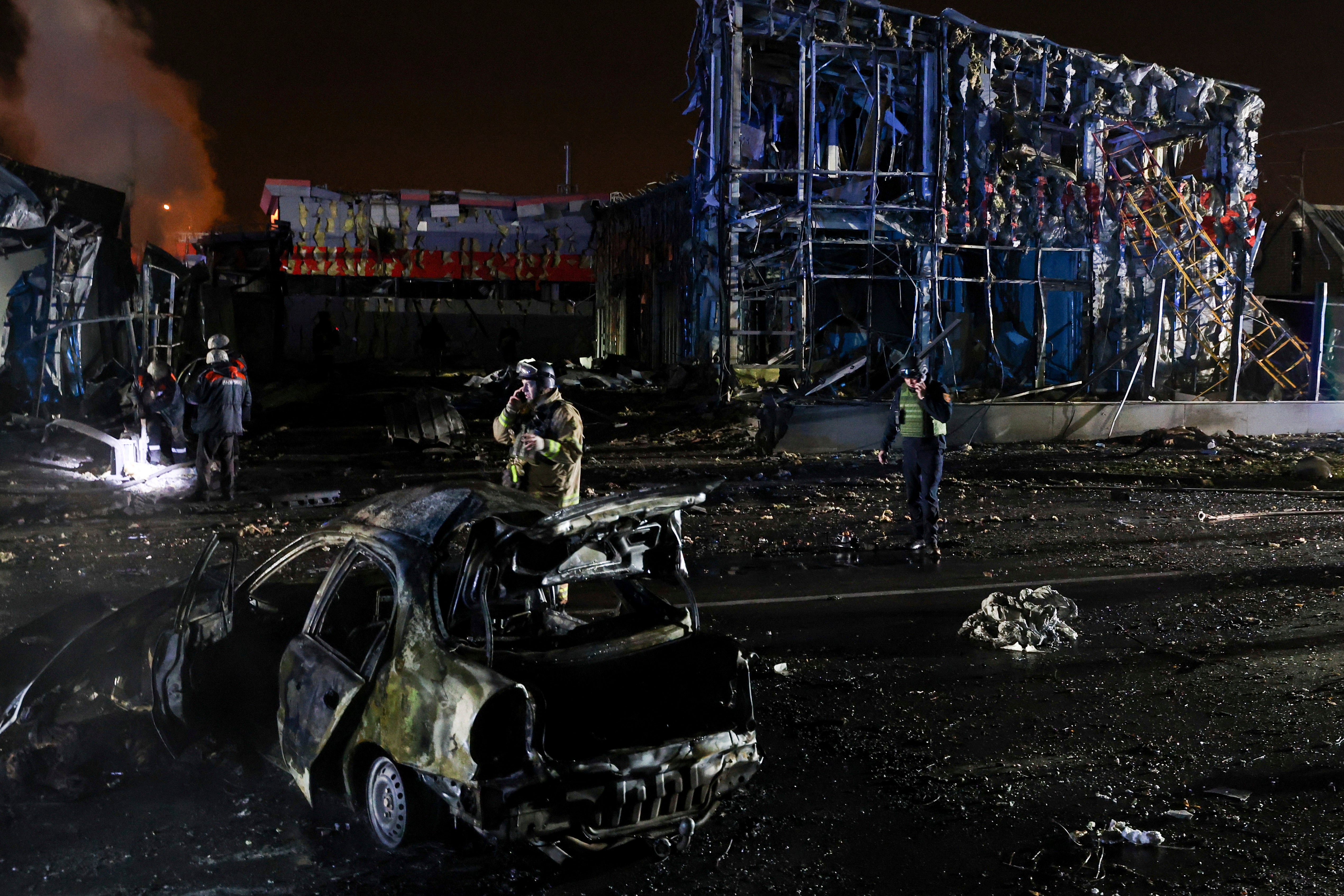 Rescue workers walk in front of a car and a building destroyed by a Russian strike in Zaporizhzhia