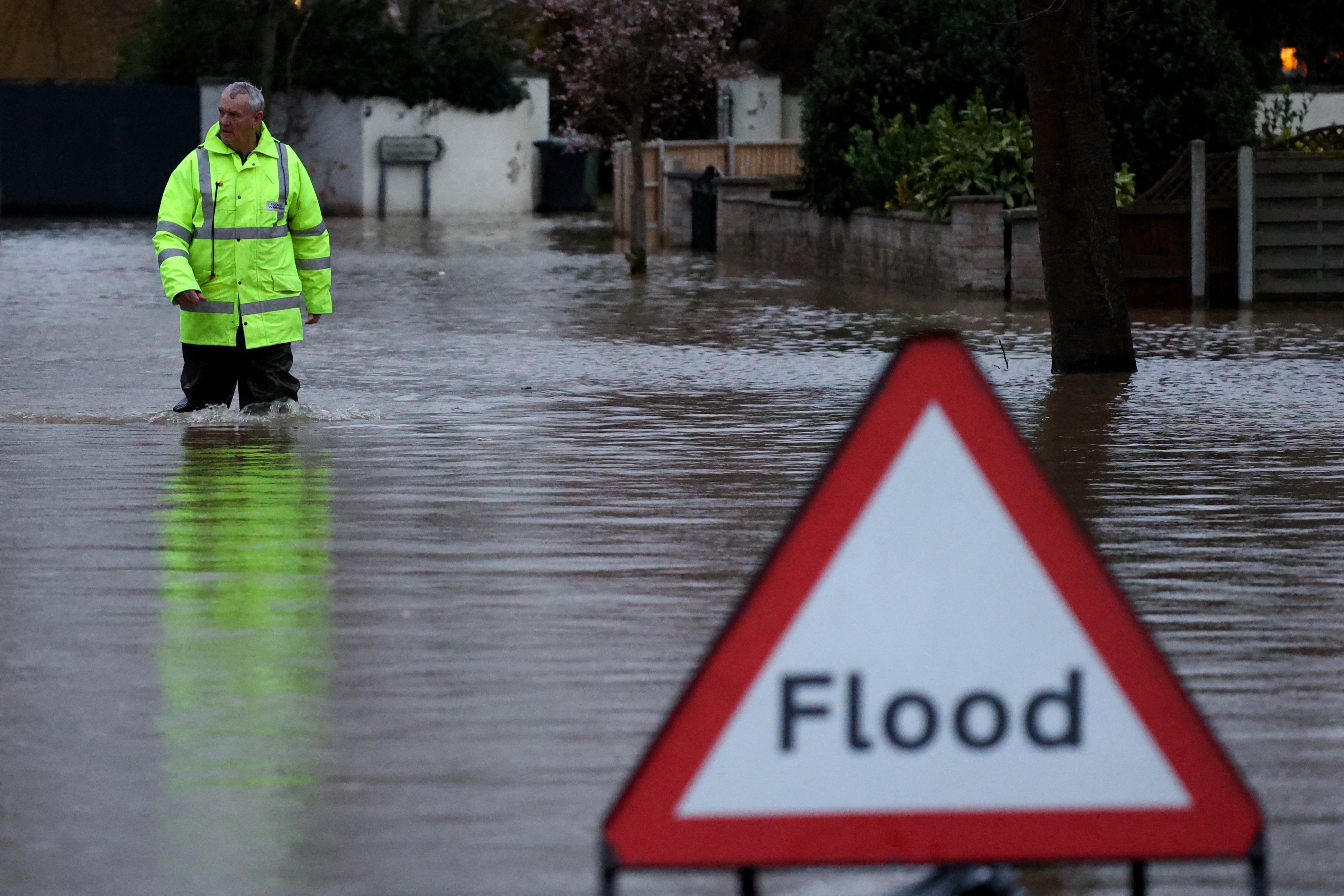 A flood warden wades in the water on a road near a warning sign after Storm Darragh hit the country, in Hereford, Britain