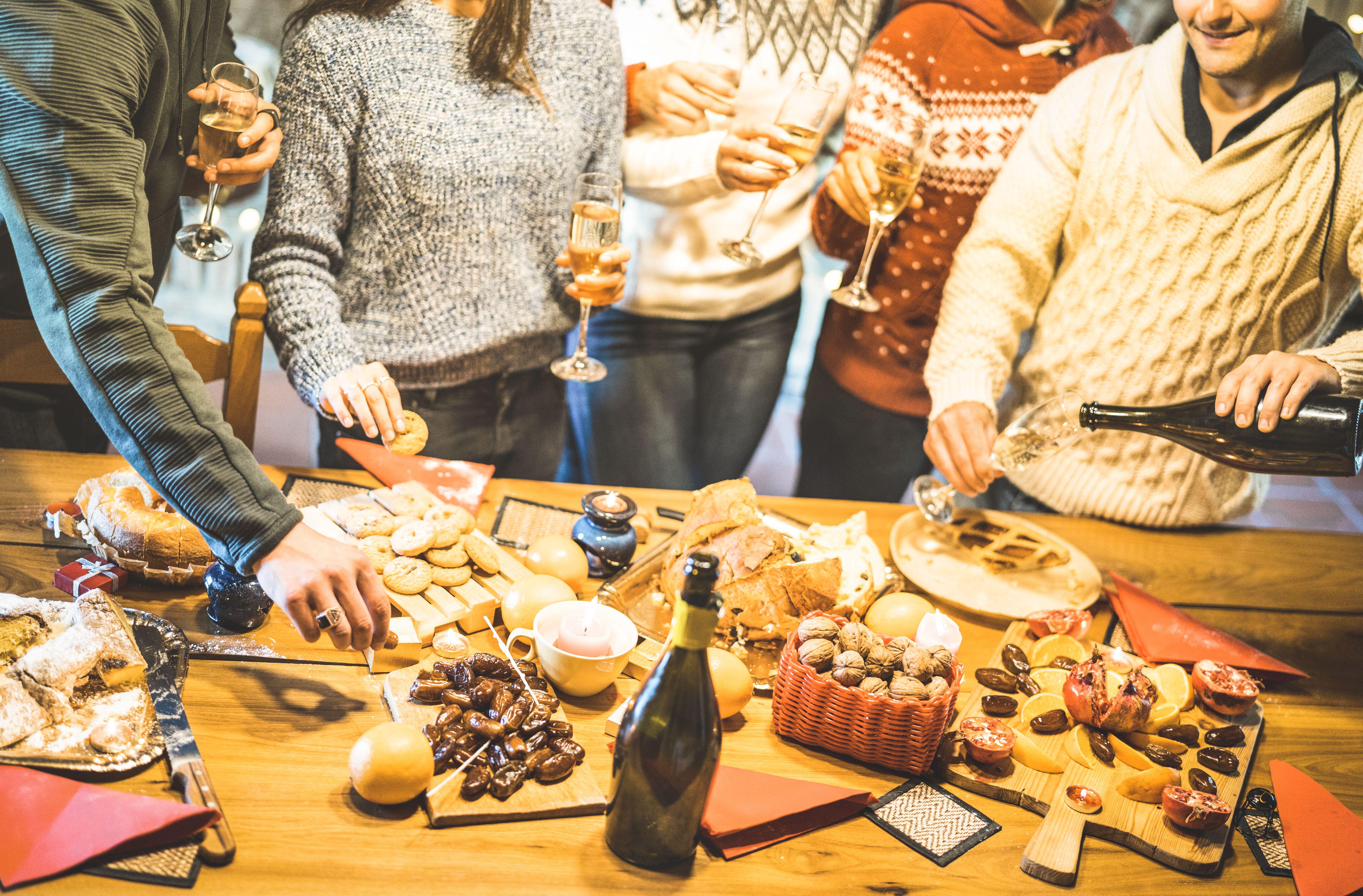 Seitenansicht einer Freundesgruppe, die Weihnachtssüßigkeiten probiert und zu Hause Spaß beim Trinken von Champagner-Sekt hat – Konzept für Winterferien