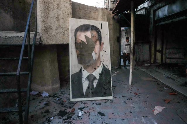 <p>A defaced portrait of ousted Syrian president Bashar al-Assad stands in a ransacked government security facility</p>