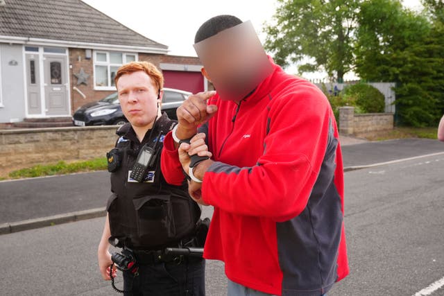 A Cleveland Police officer escorts a man arrested in Middlesbrough during a day of action following disorder in August. Image blurred at request of police (Owen Humphreys/PA)