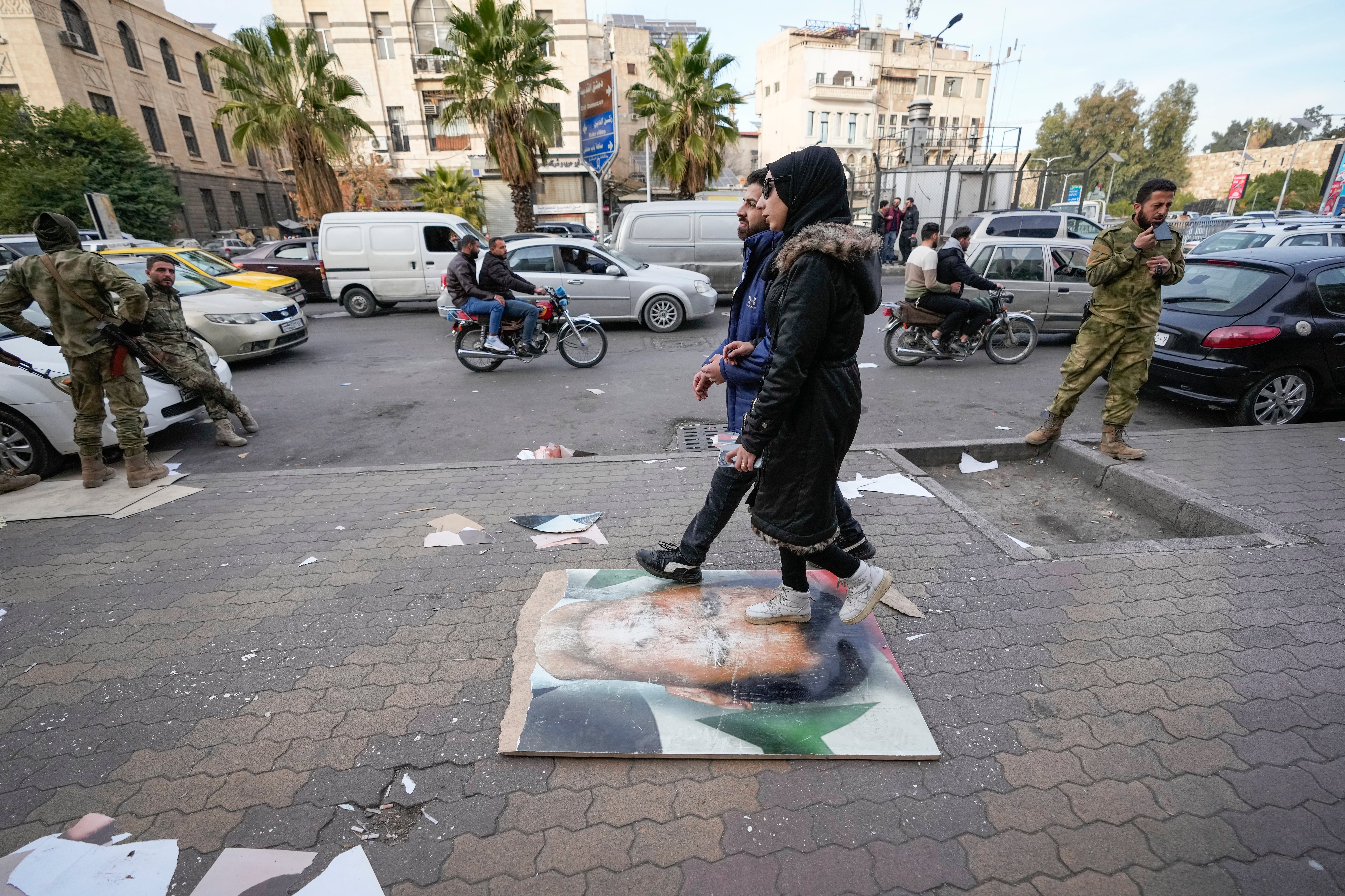 Pedestrians casually walk over an image of former Syrian President Bashar Assad on a sidewalk in Damascus, Syria, Tuesday, Dec. 10, 2024.