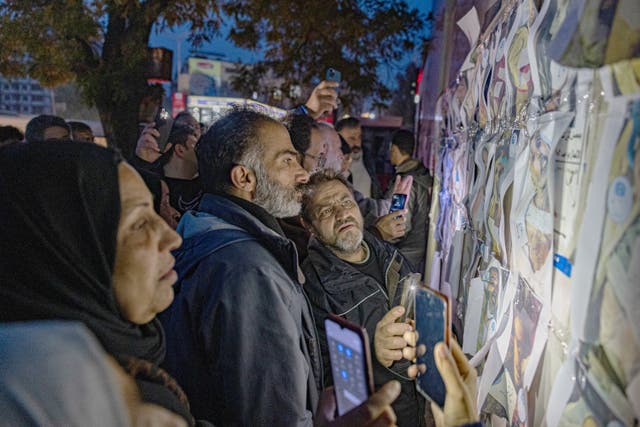 <p>Outside a morgue in Damascus, relatives check pictures of bodies in the search for loved ones</p>