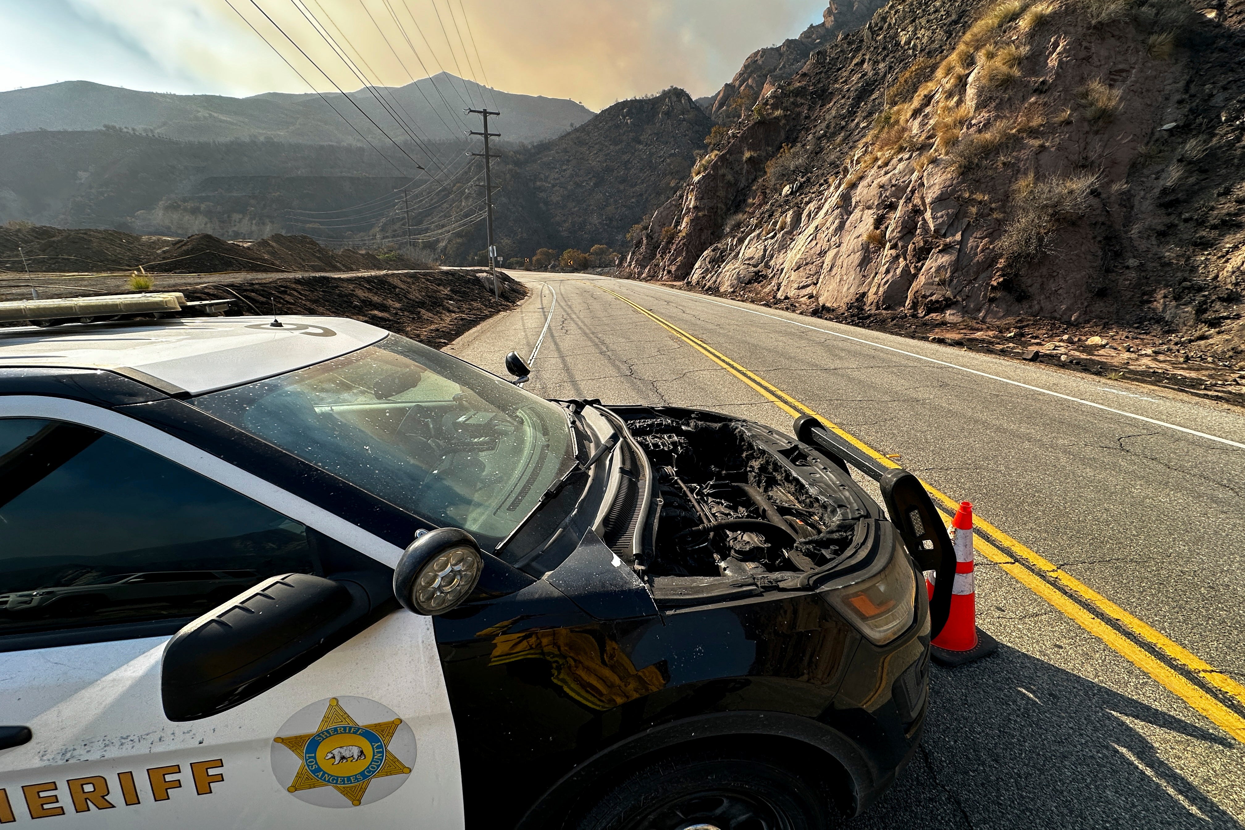 A fire-damaged police vehicle sits on Malibu Canyon Road on Tuesday in Malibu, California. The road was closed to the public