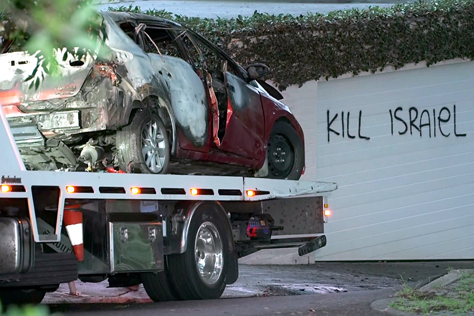 A torched car being removed in front of anti-Israel graffiti written on a wall in the Sydney suburb of Woollahra