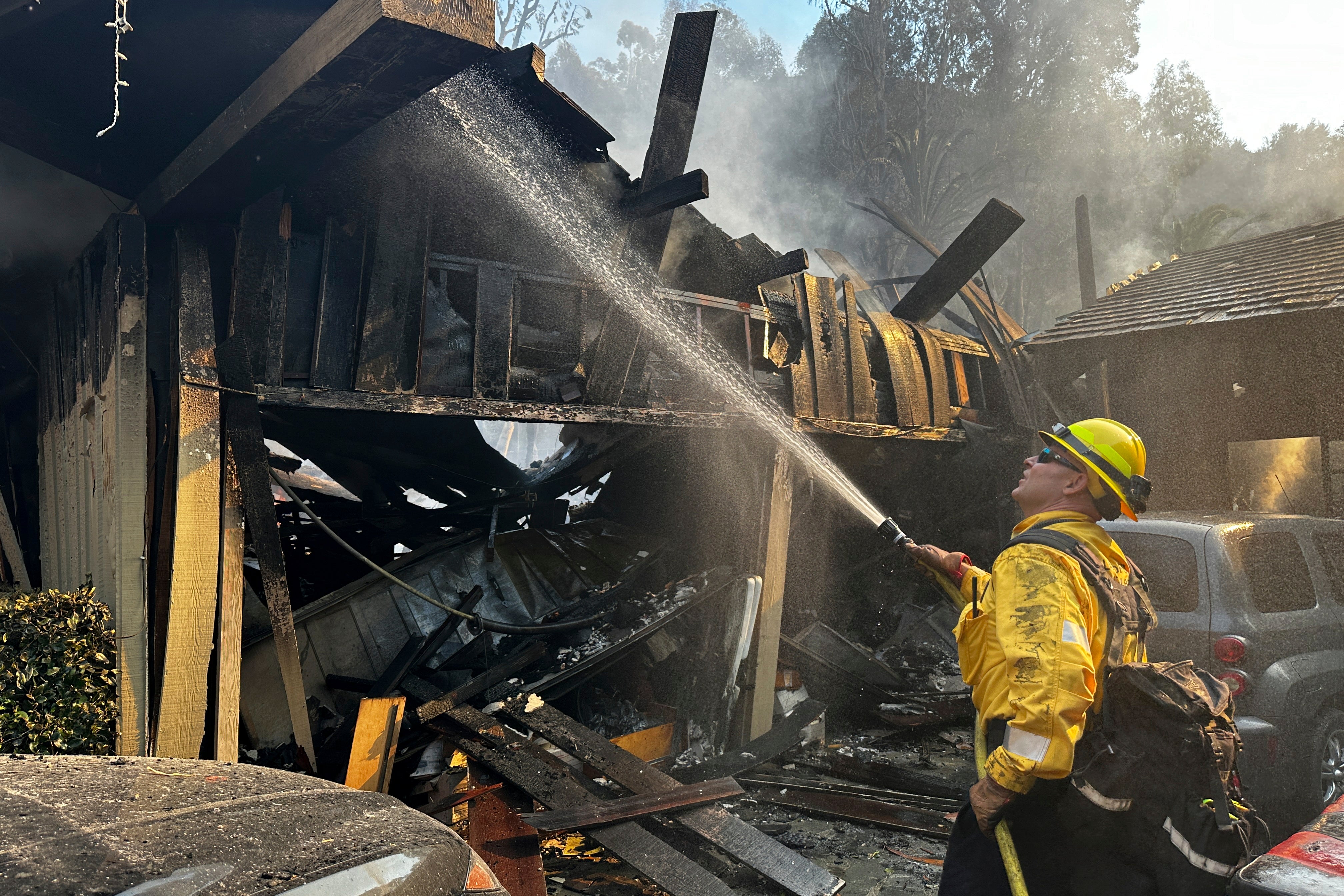 A firefighter hoses down hot spots around a fire-ravaged property after the Franklin Fire swept through Malibu