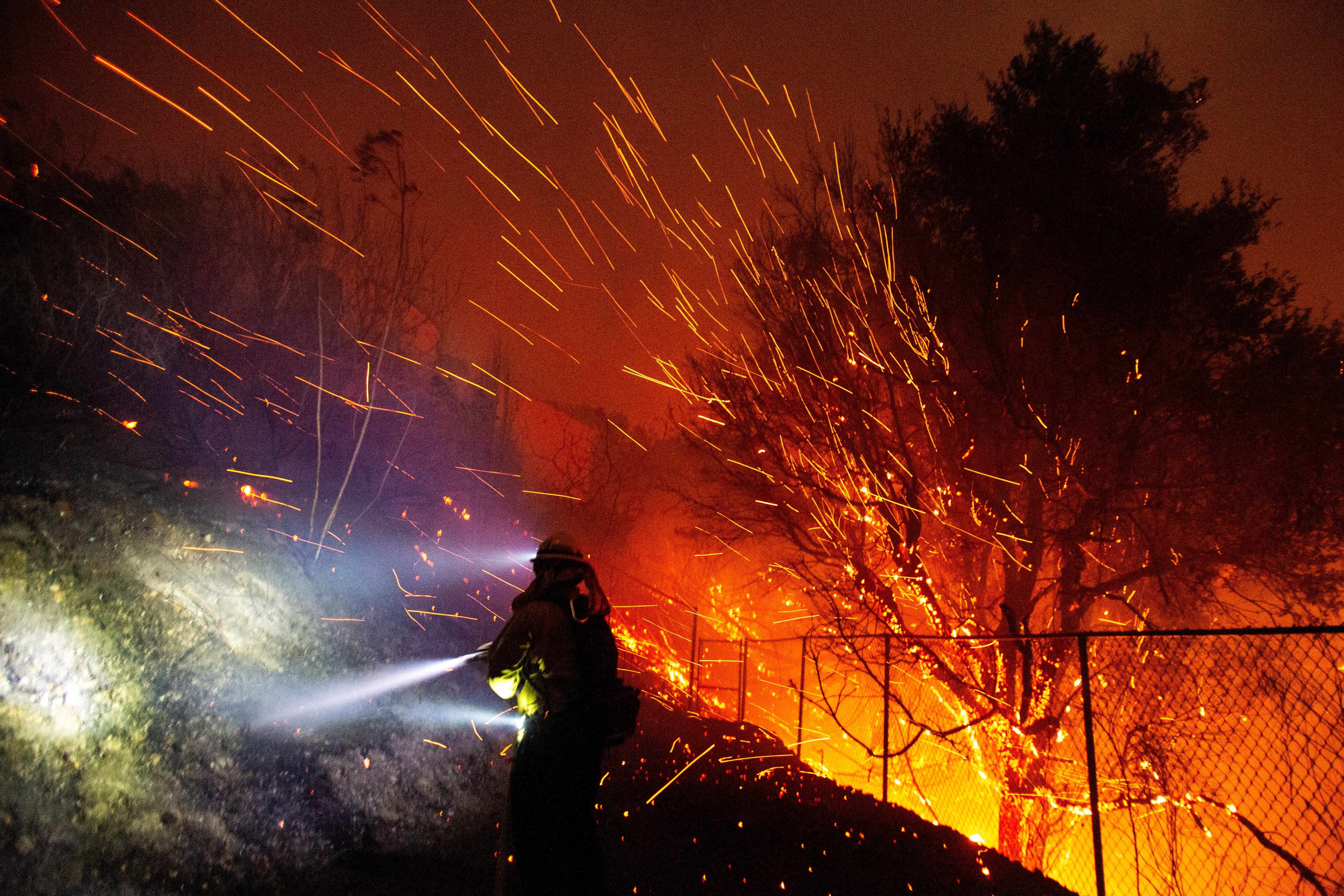 Wind whips embers from the trees while a firefighter works Tuesday amid the Franklin Fire in Malibu, California. The wildfire has spread quickly over the past day