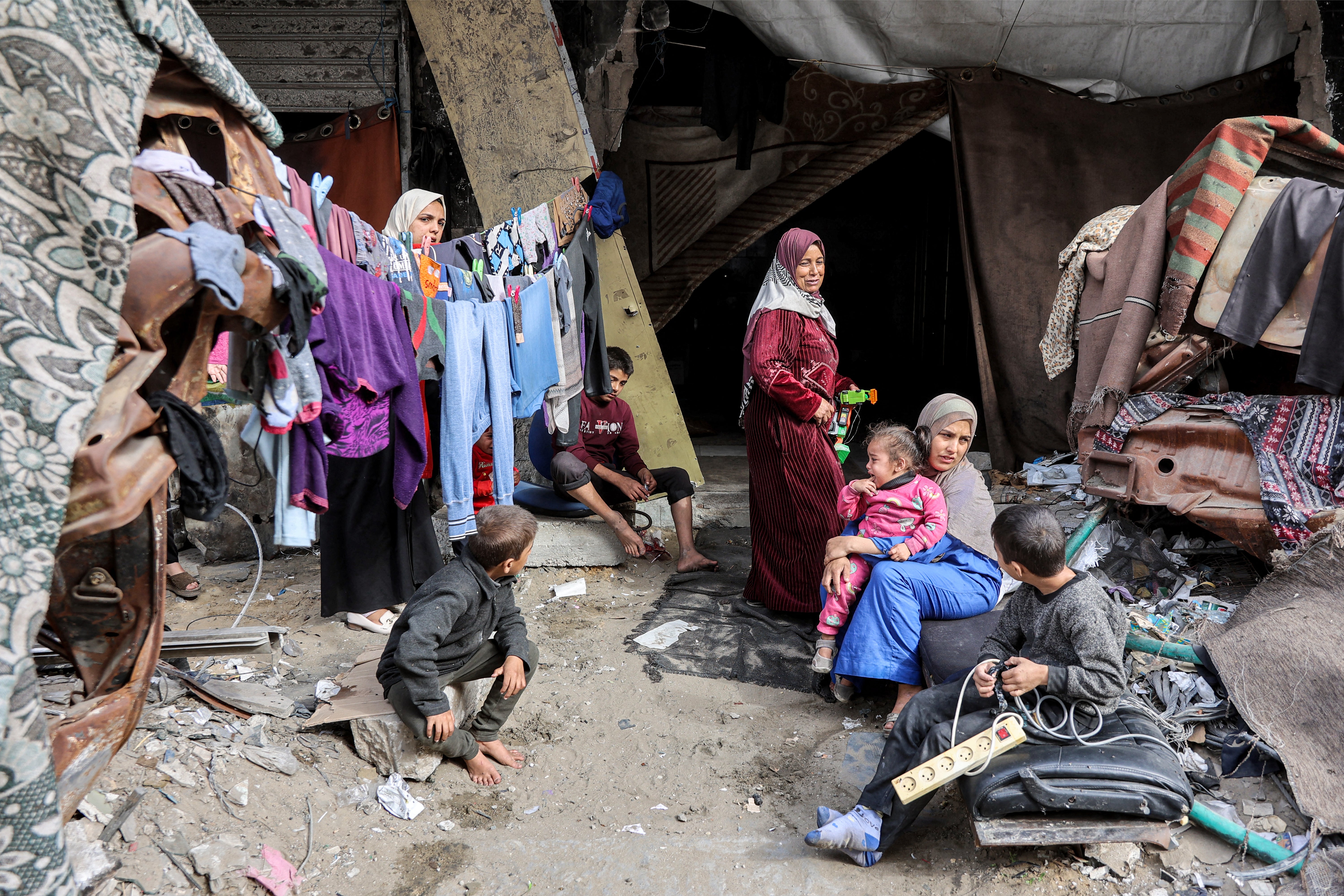 Women and children sit and walk near clothes drying on a laundry line at a shelter for displaced Palestinians in Gaza City on 11 December 2024 amid the ongoing war in the Palestinian territory between Israel and Hamas