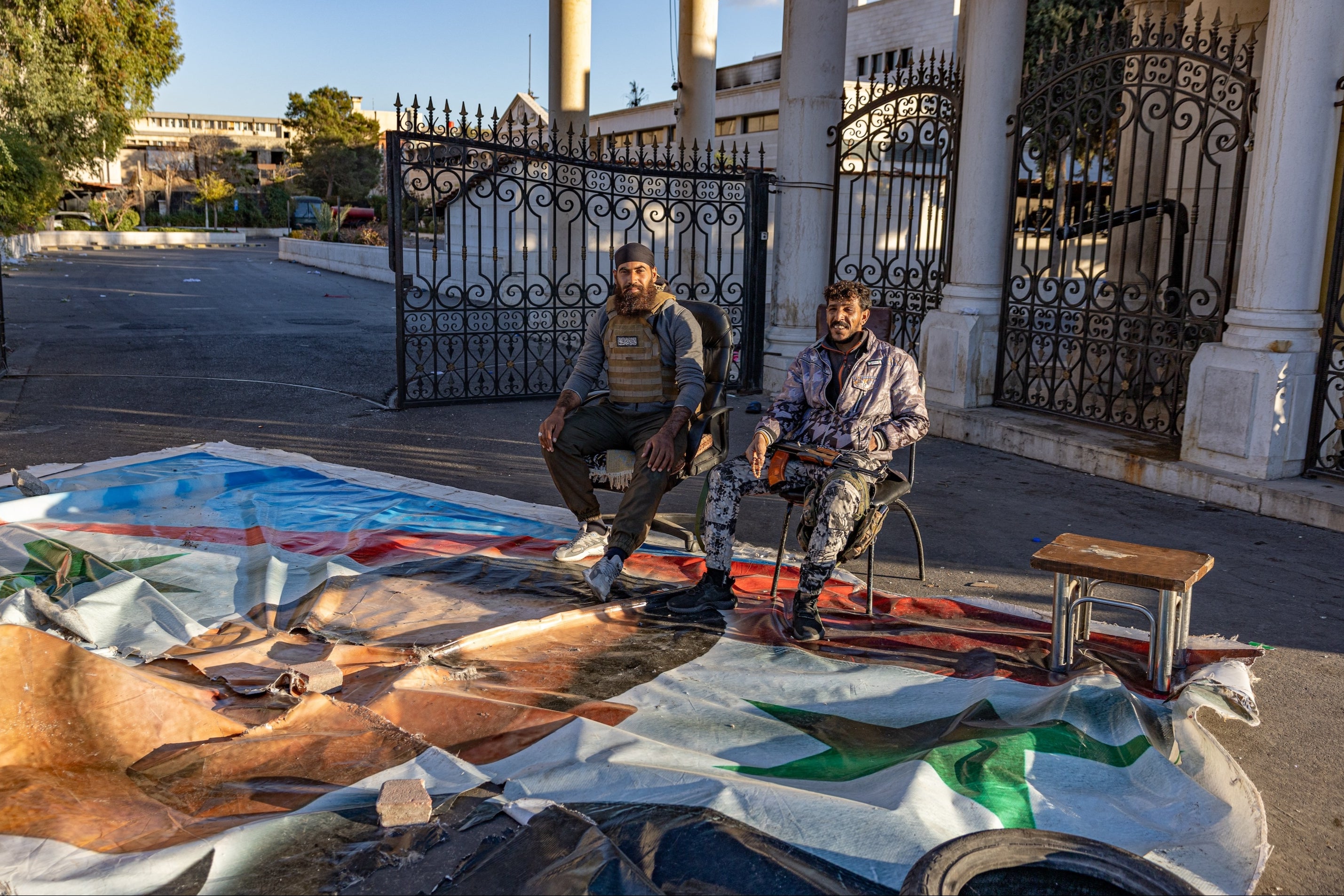 Two foot soldiers sitting on a portrait of Assad outside the military judicial building