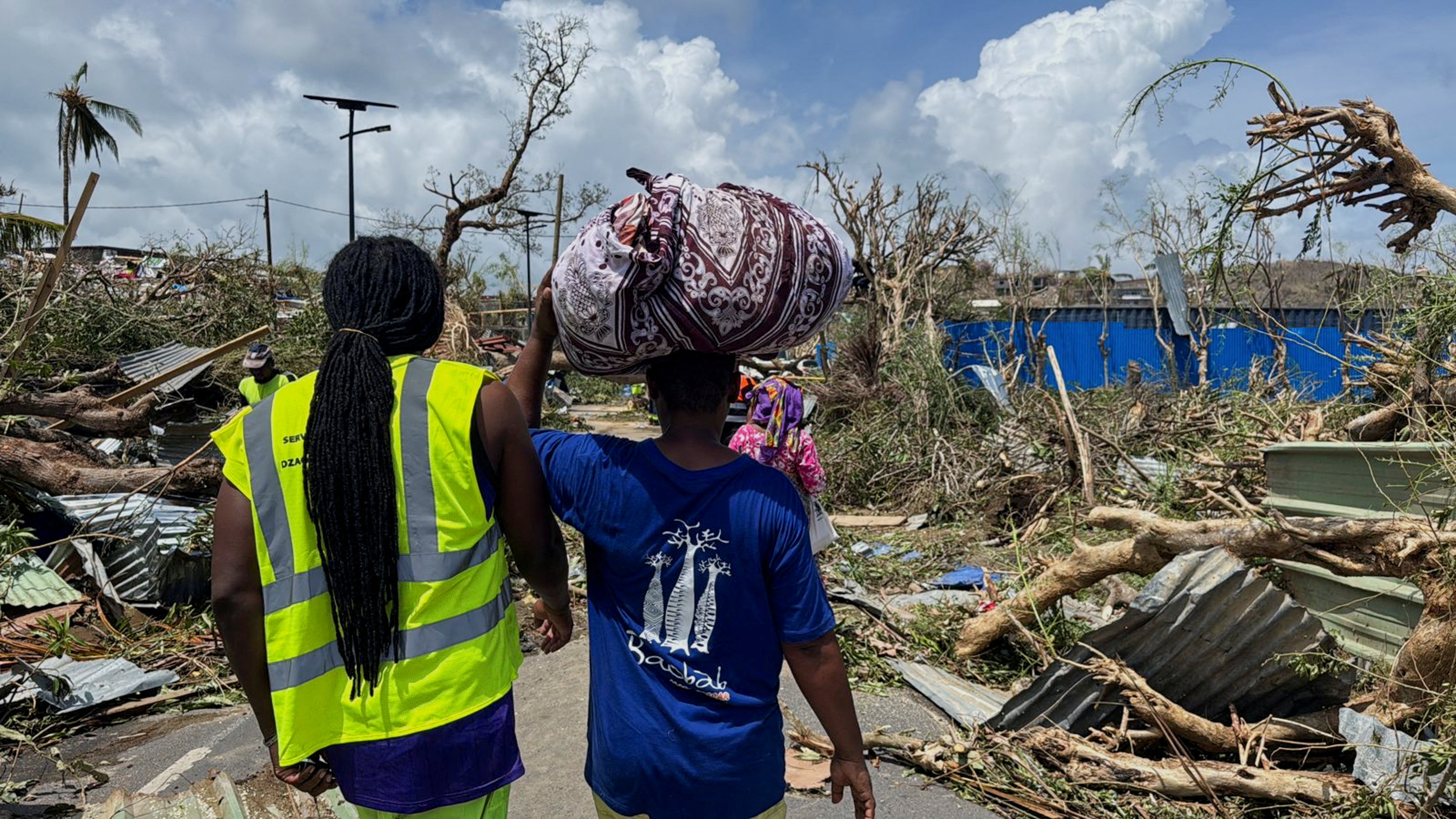 A man carries his belongings as rescue workers attempt to clear a blocked road, in the aftermath of Cyclone Chido, within Labattoir, in Mayotte, France