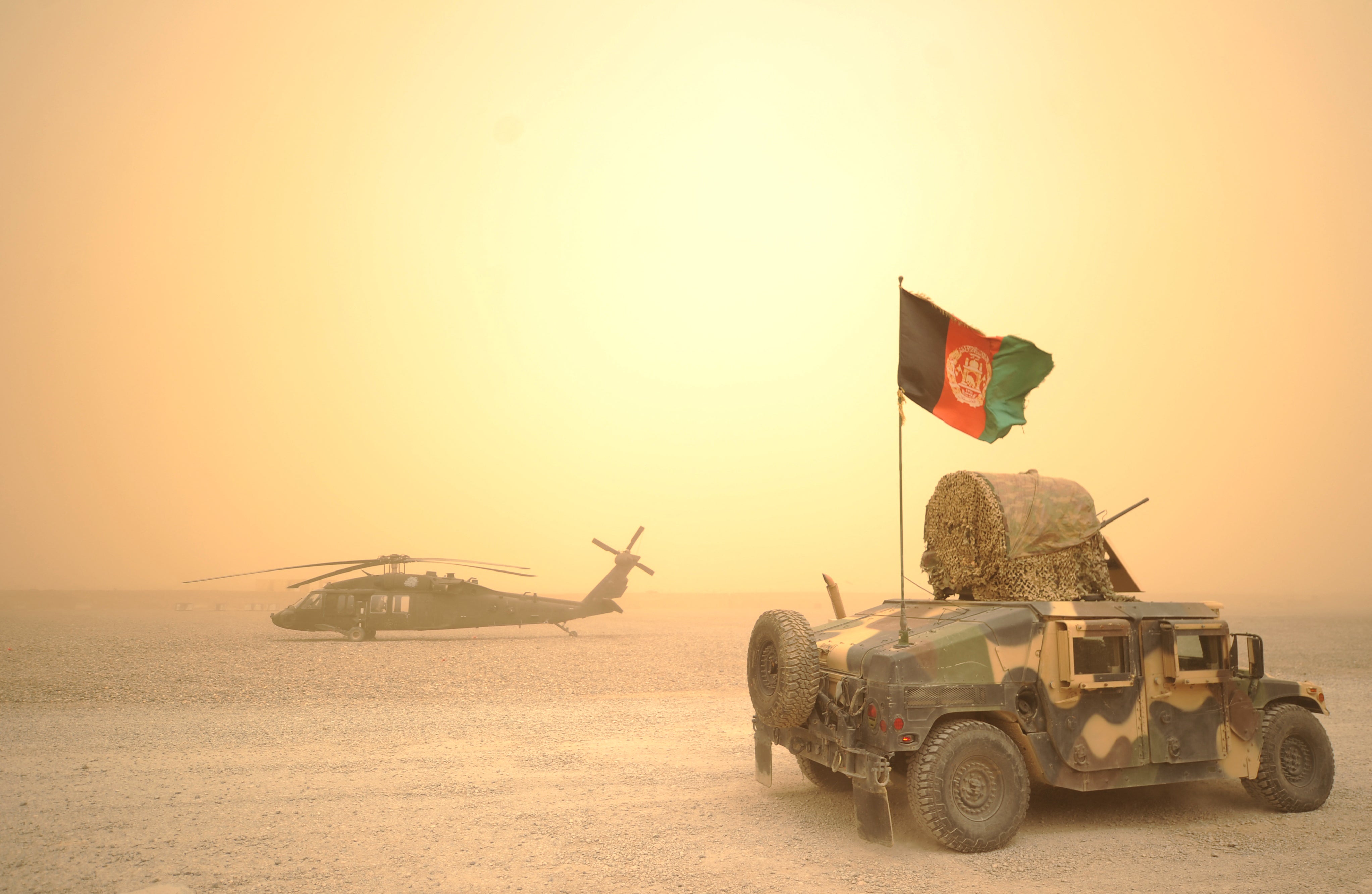 An Afghan National Army Humvee jeep drives past a US army Blackhawk helicopter during a sandstorm at FOB Wilson in Kandahar