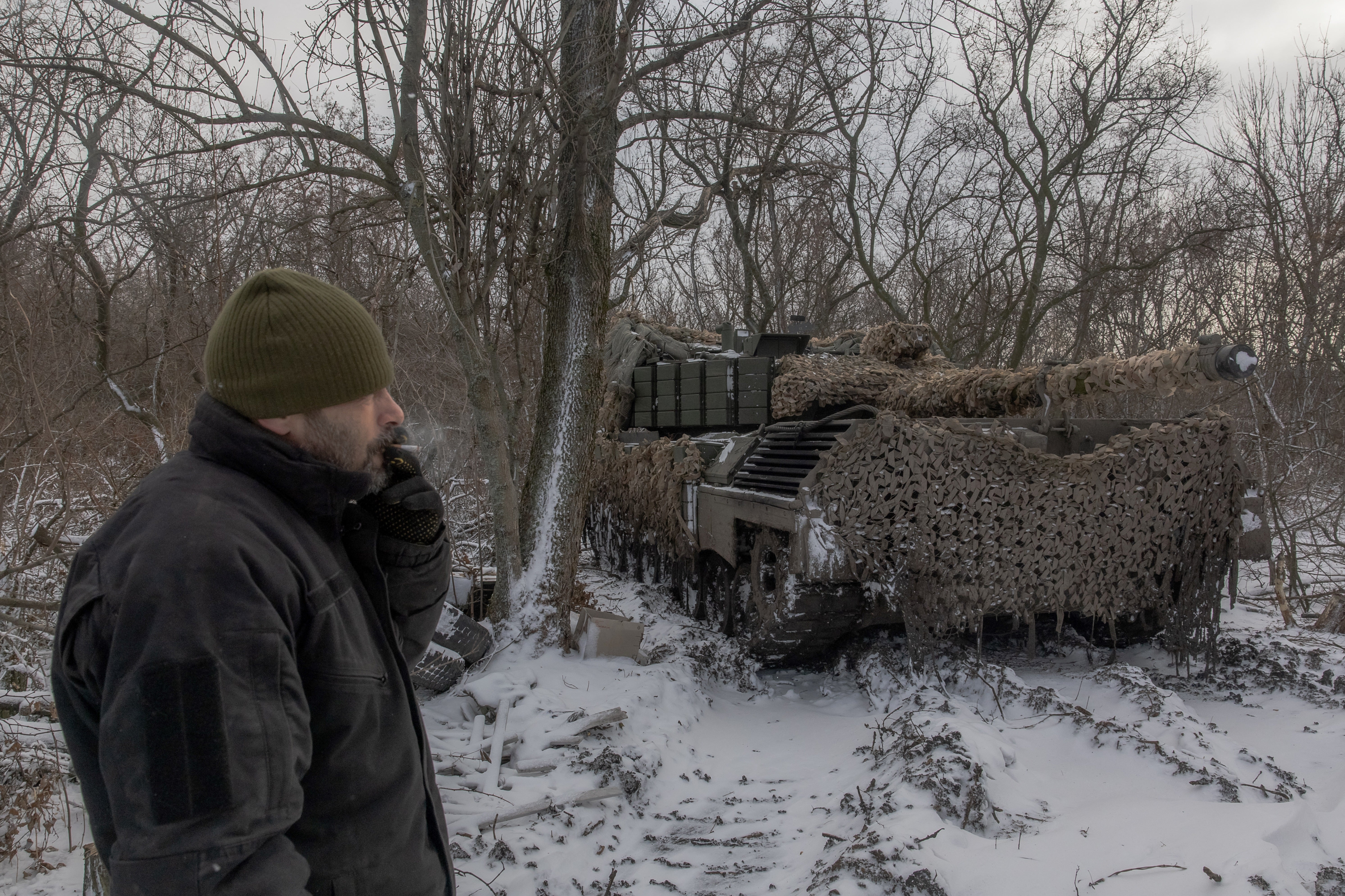 A Ukrainian tank crew member smokes a cigarette next to a Leopard 1A5 tank