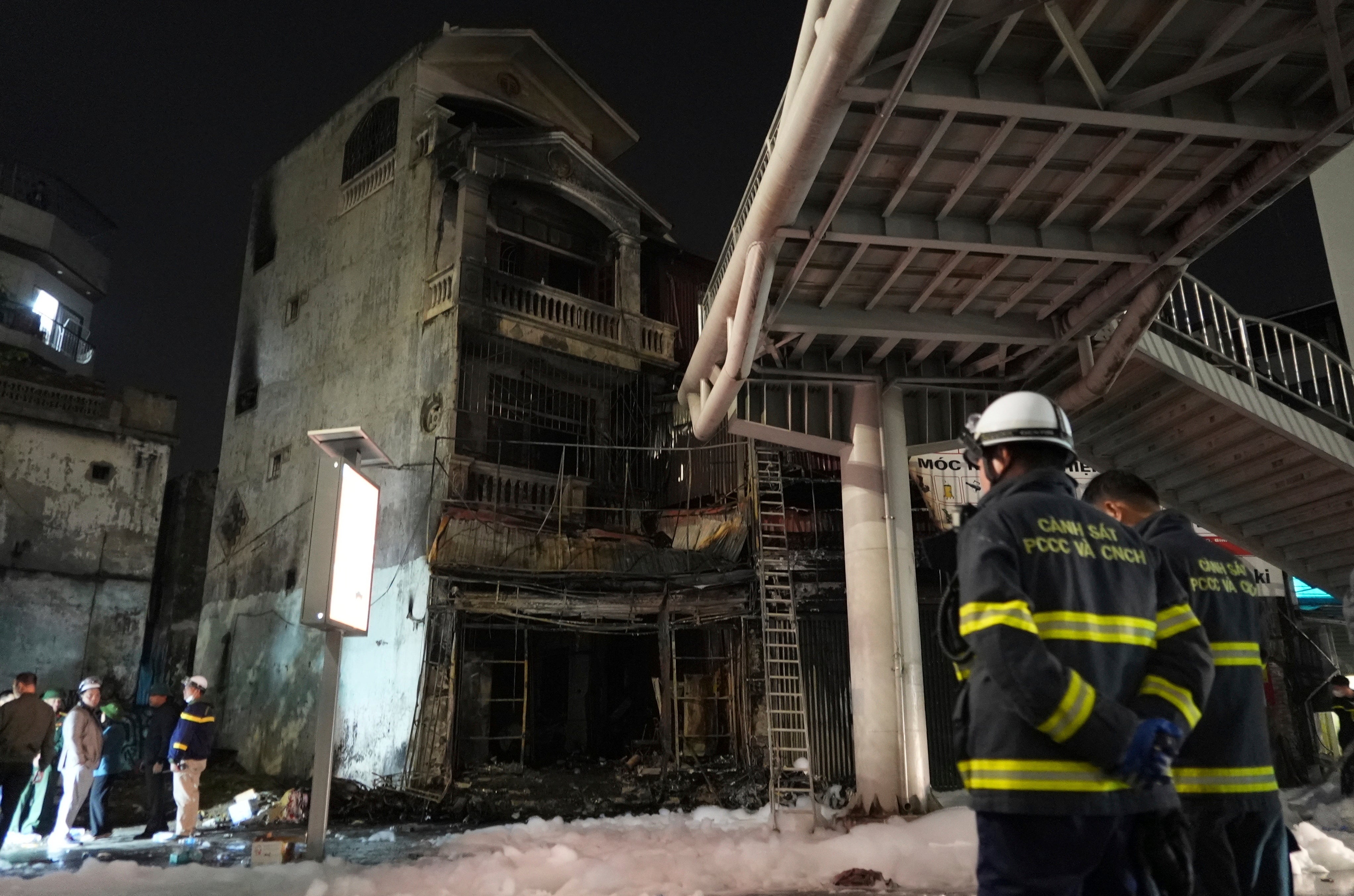 Firemen stand in front of a building burned down by fire in Hanoi, Vietnam on Thursday