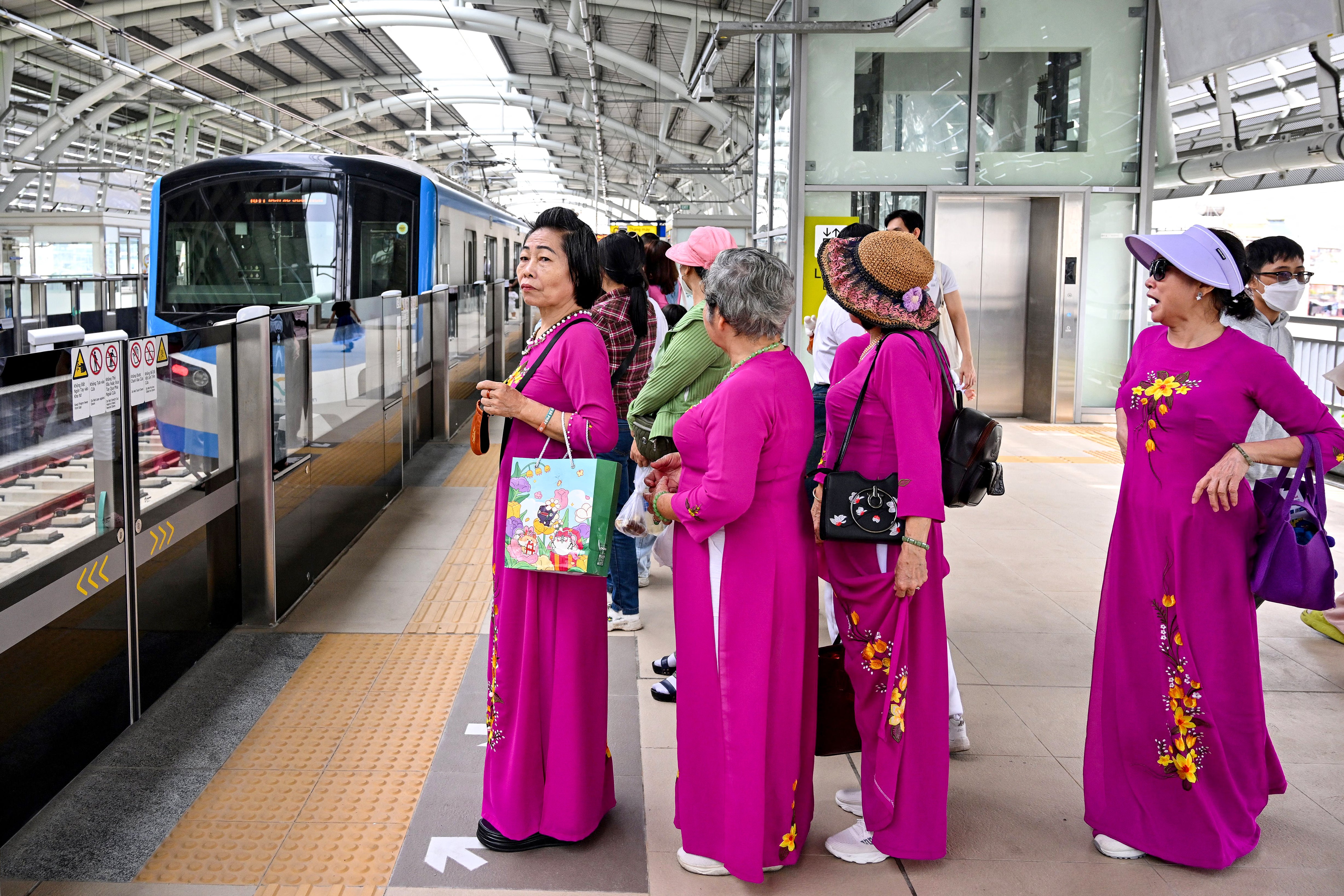 Women in traditional ‘ao dai’ dress as they wait to board a train on the platform at a metro station in Ho Chi Minh City on 22 December 2024. Thousands of selfie-taking Ho Chi Minh City residents crammed into train carriages on 22 December, as the traffic-clogged business hub celebrated the opening of its first-ever metro line after years of delays