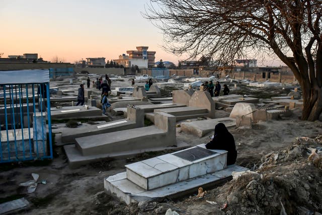 <p>An Afghan woman sits next to a grave reciting the holy Koran at a cemetery on the outskirts of Mazar-i-Sharif in Balkh province</p>