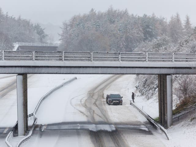 <p>A person stands next to his vehicle on an empty snow-covered M9 motorway near Stirling (Robert Perry/PA)</p>