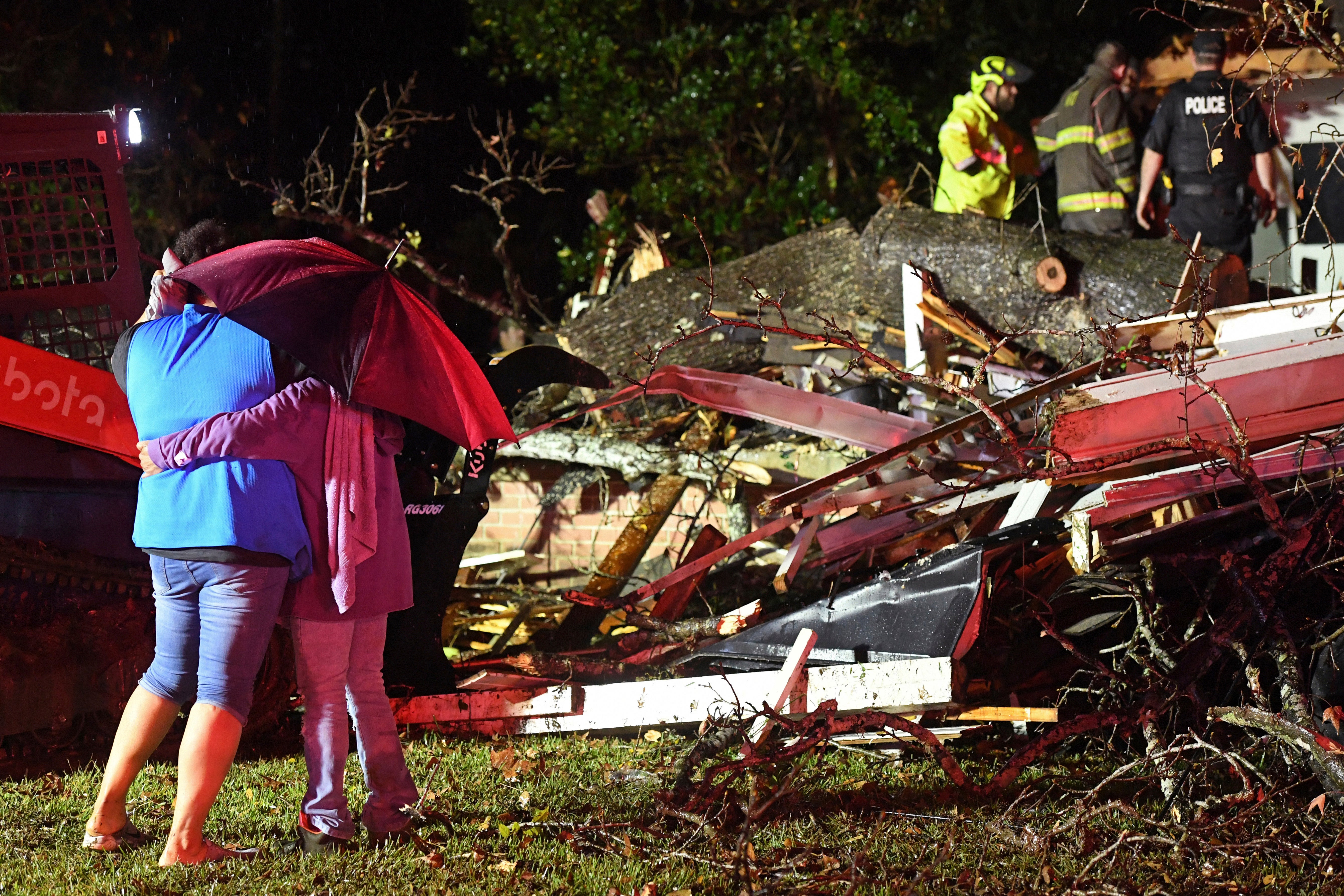 Bystanders hug as first responders work to free a victim after a tree fell on a house in Mississippi