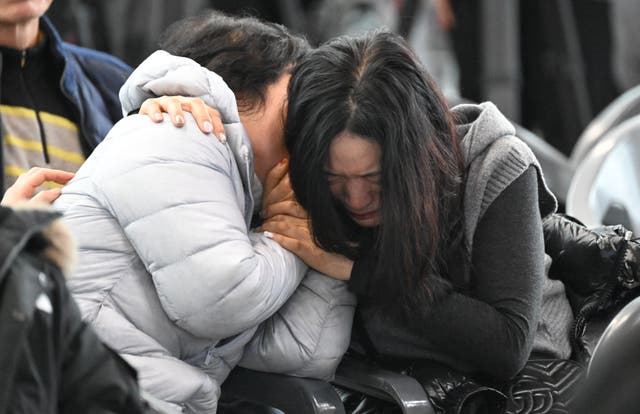 <p>Two women in Muan International hold each other as names of the dead are read out </p>