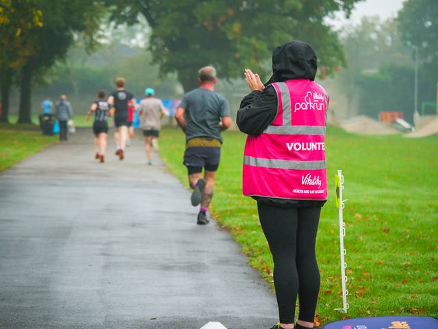 <p>A volunteer helps Parkrun competitors</p>