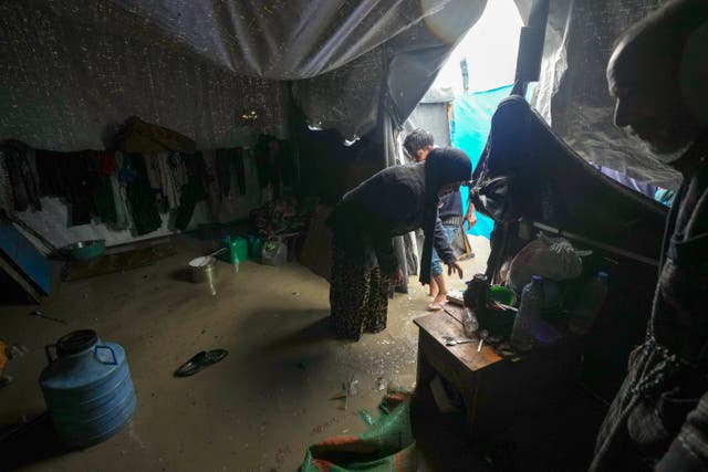<p>Manal Lubbad, a mother of eight displaced from Gaza City, tries to clean her flooded tent after heavy overnight rainfall at the refugee camp in Deir al-Balah </p>
