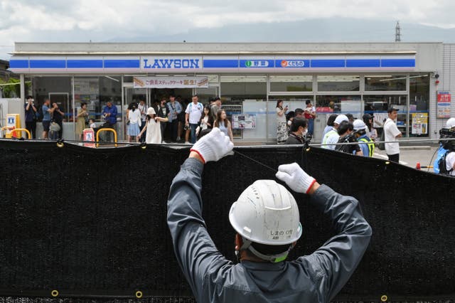 <p>A worker installs a barrier to block the sight of Mount Fuji emerging from behind a convenience store to deter badly behaved tourists, in the town of Fujikawaguchiko</p>