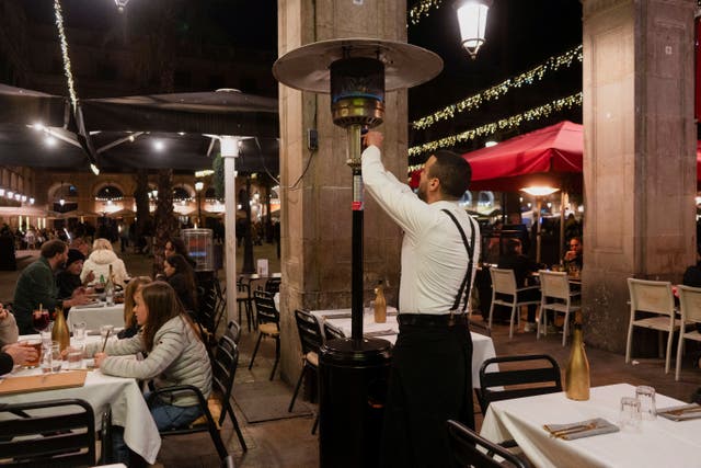 <p>A waiter turns on a gas heater while tourists sit on a terrace</p>