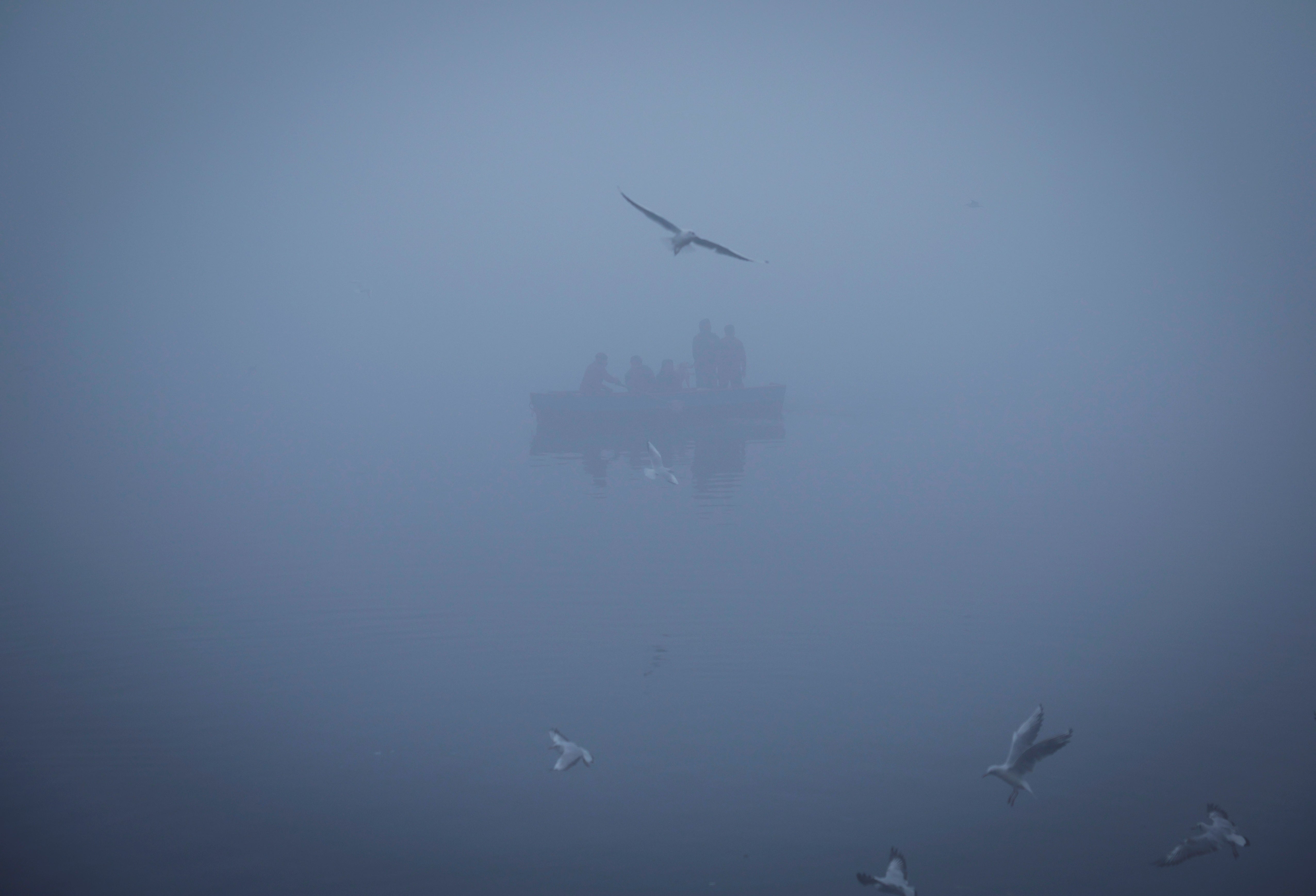 People ride a boat across the Yamuna river on a foggy winter morning in New Delhi