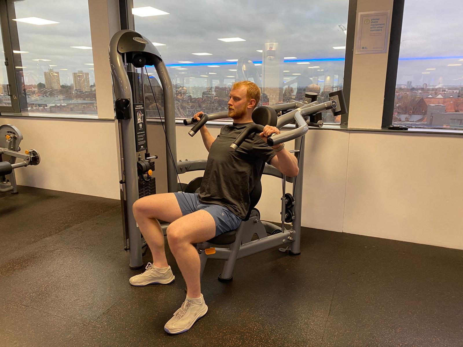 Harry Bullmore completing a set on the shoulder press machine at The Gym Group, Wood Green The Mall