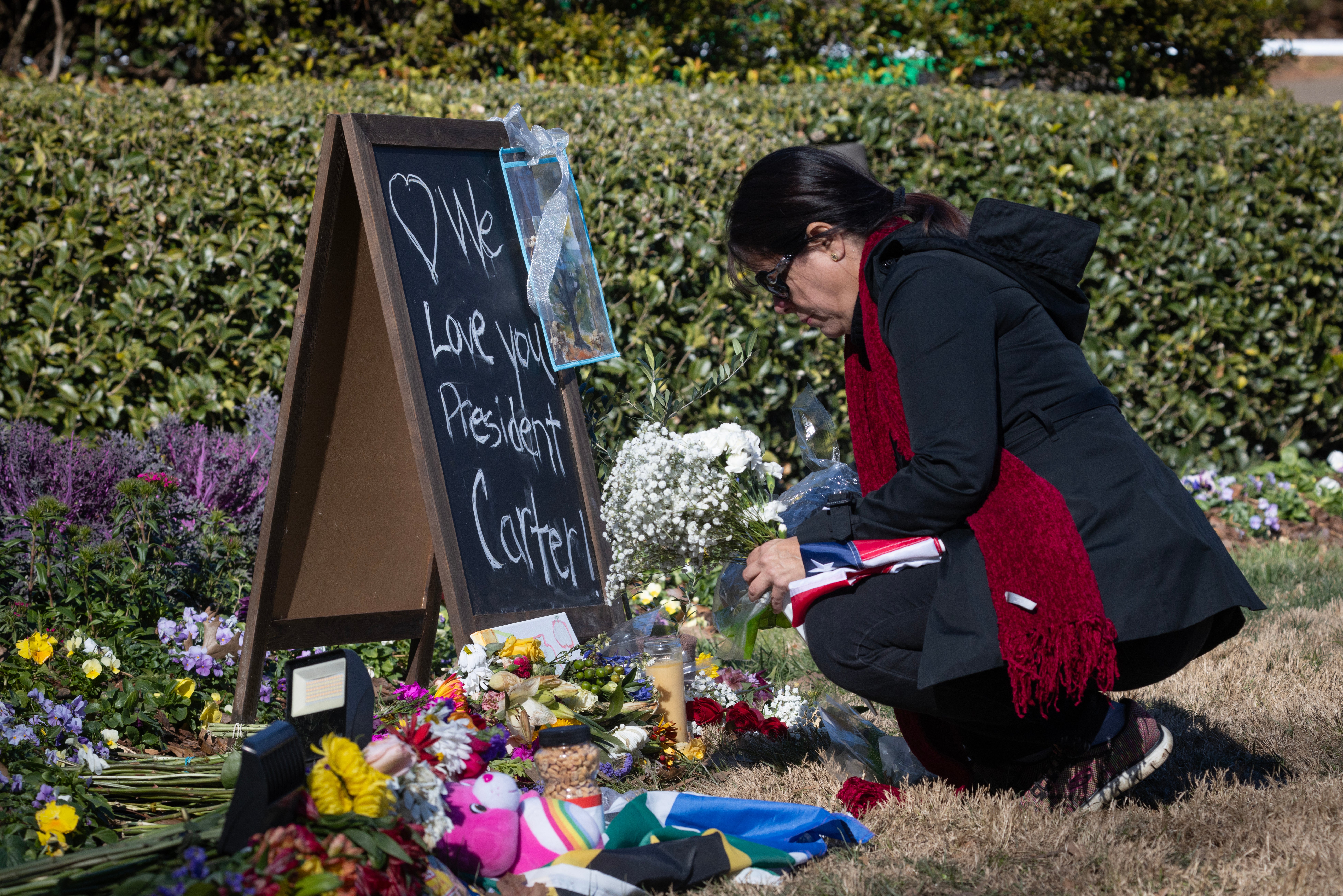 A mourner places flowers outside the Carter Center. Former president Jimmy Carter’s hearse is set to arrive in Atlanta this afternoon