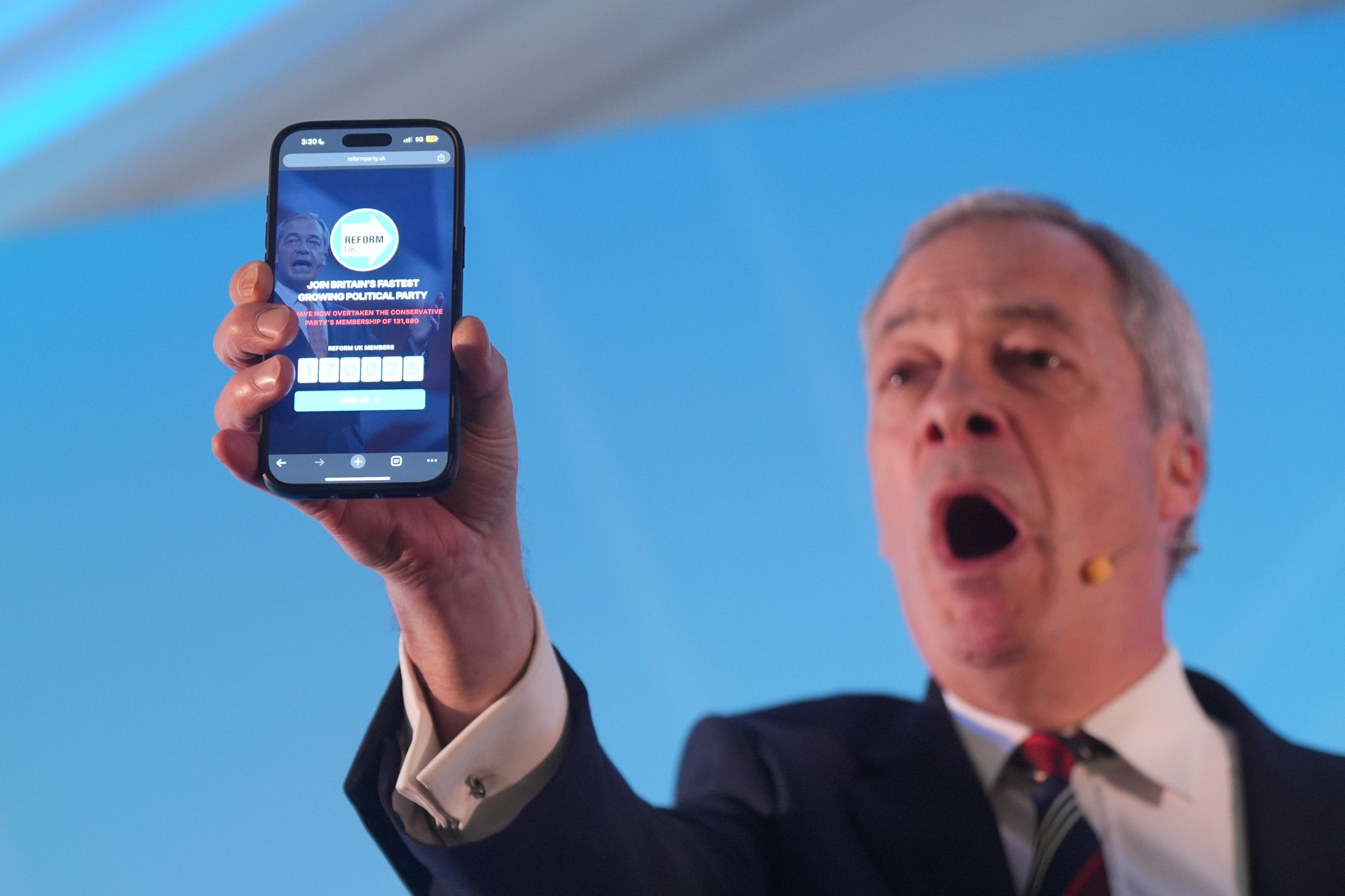 Nigel Farage held up a phone displaying the number of Reform UK party members whilst speaking at his party’s East of England conference at Chelmsford City Racecourse in Essex (Yui Mok/PA)