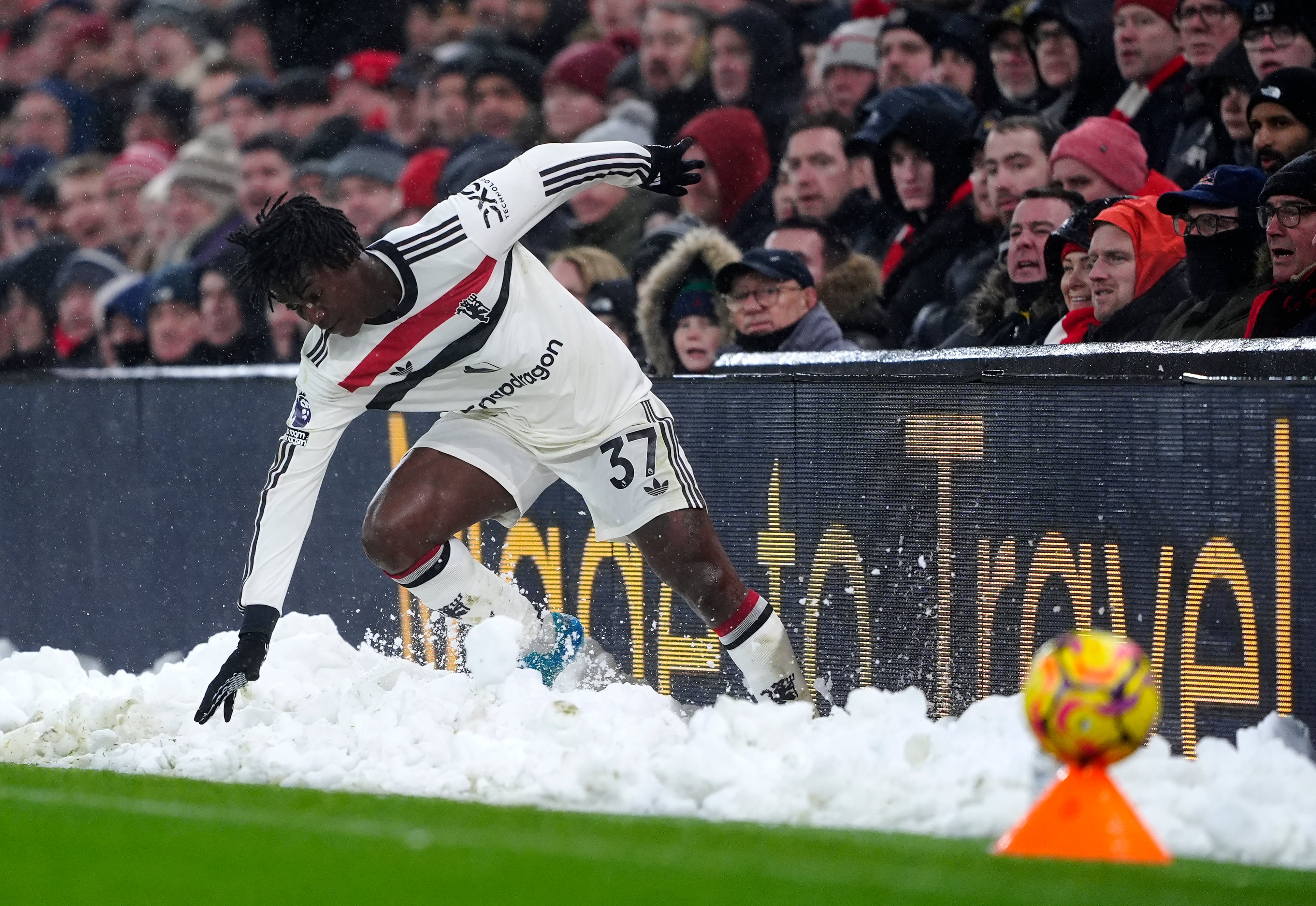 Manchester United's Kobbie Mainoo slides into a bank of snow on the touchline at Anfield, Liverpool, on Sunday