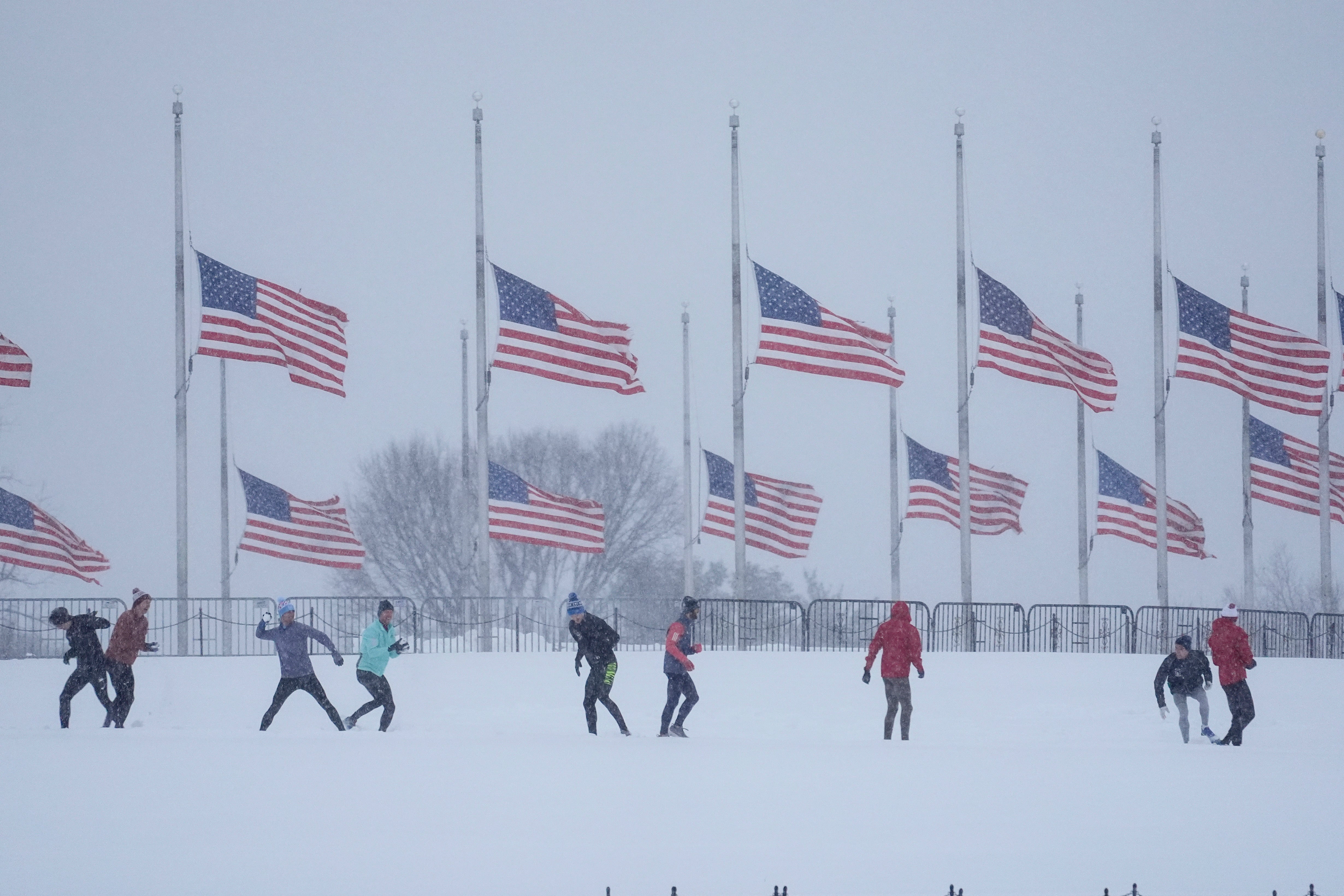 People throw snowballs on Monday near D.C.’s Washington Monument as U.S. flags fly at half-staff in memorial to former President Jimmy Carter. The city will see several inches of snow