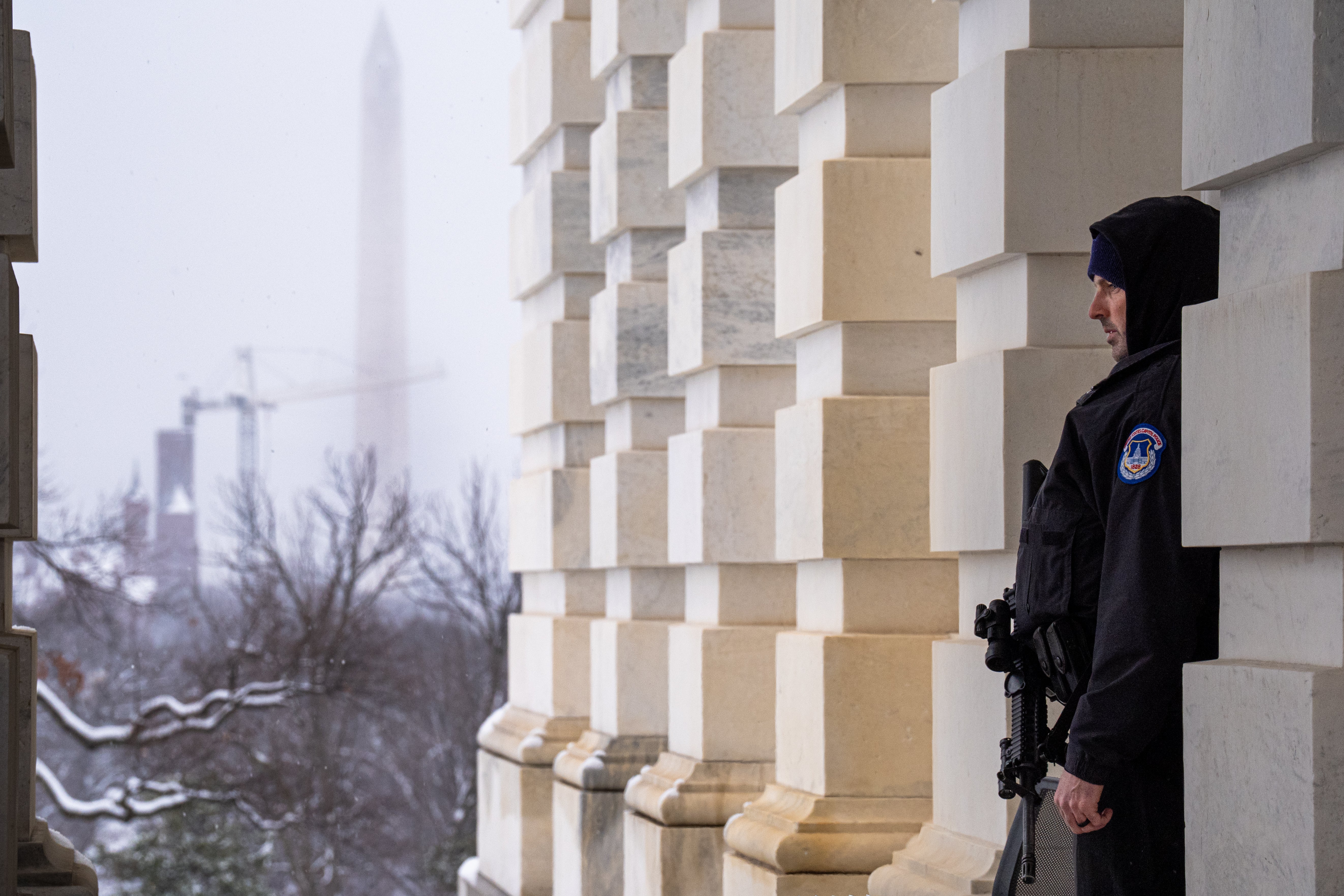 The Washington Monument is visible as a U.S. Capitol Police officer stands guard at the U.S. Capitol Building on Monday. Snow from the winter storm is seen falling outside. The area will see several inches before the day is done