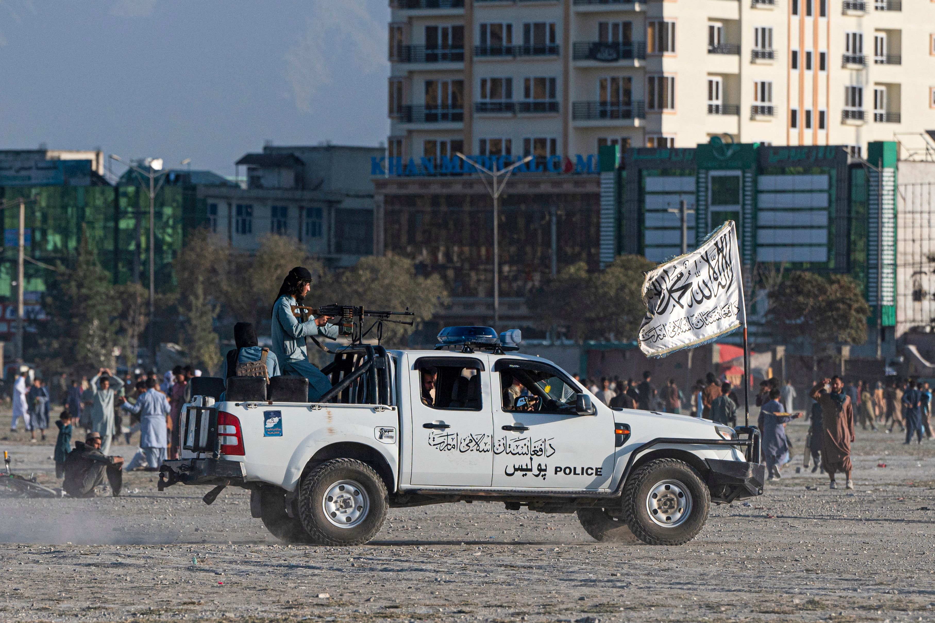 Taliban fighters ride a vehicle as Afghan men play cricket at the Chaman-e-Huzuri ground in Kabul