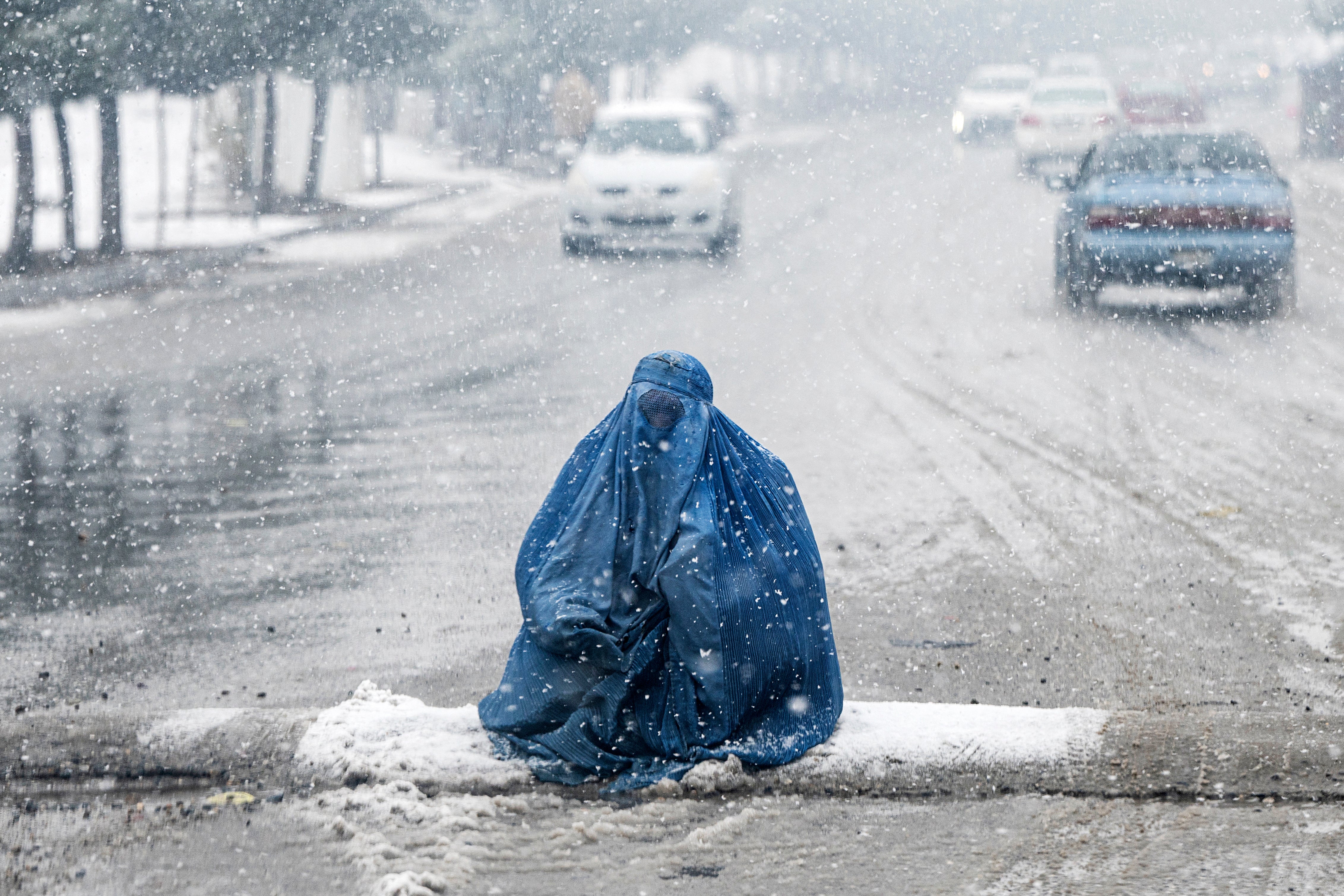 An Afghan burqa-clad woman looks for alms along a street, during the first heavy snowfall this winter in Kabul