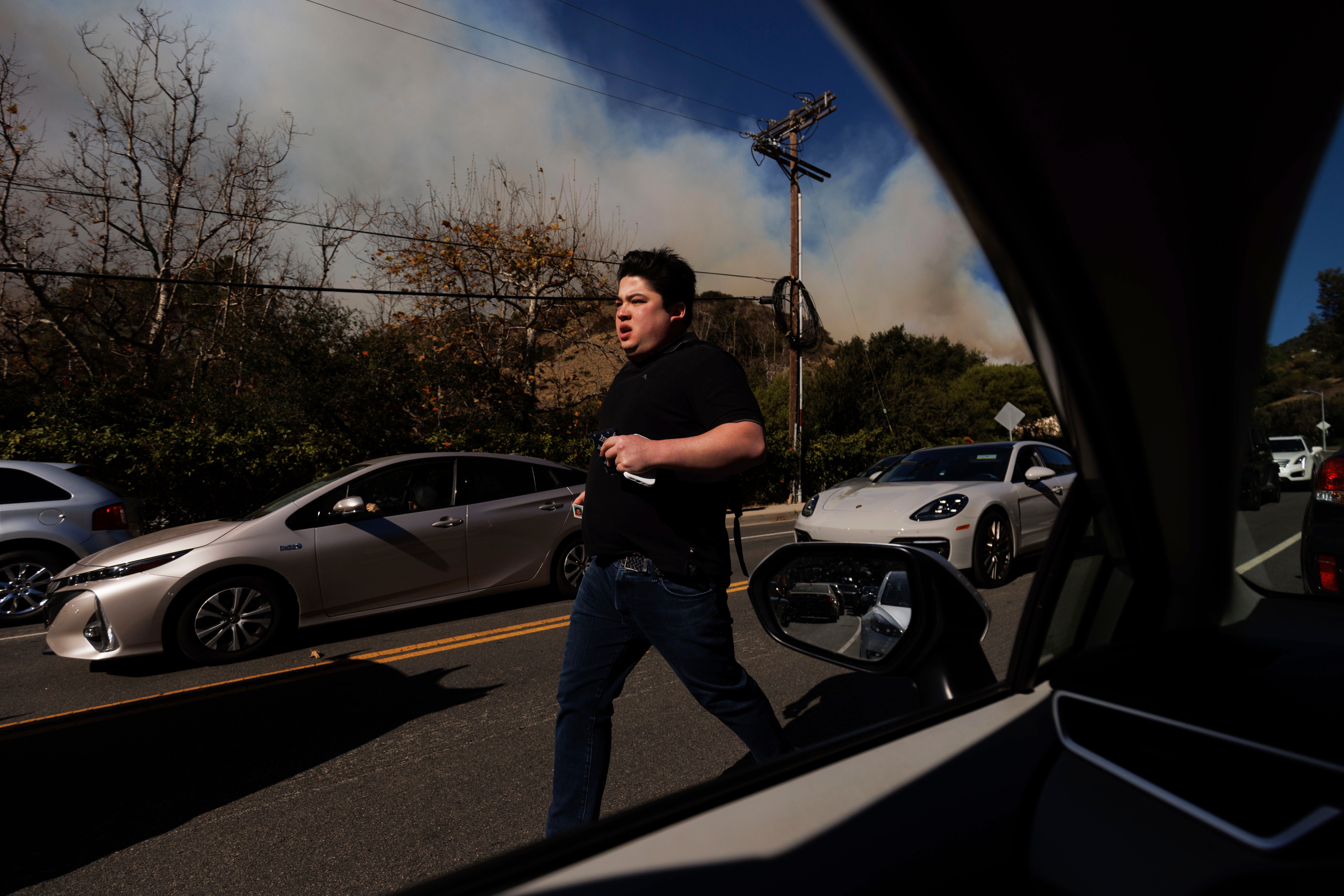 A person flees from an advancing wildfire in the Pacific Palisades neighborhood of Los Angeles on Tuesday. Multiple roads were closed due to the brush fire