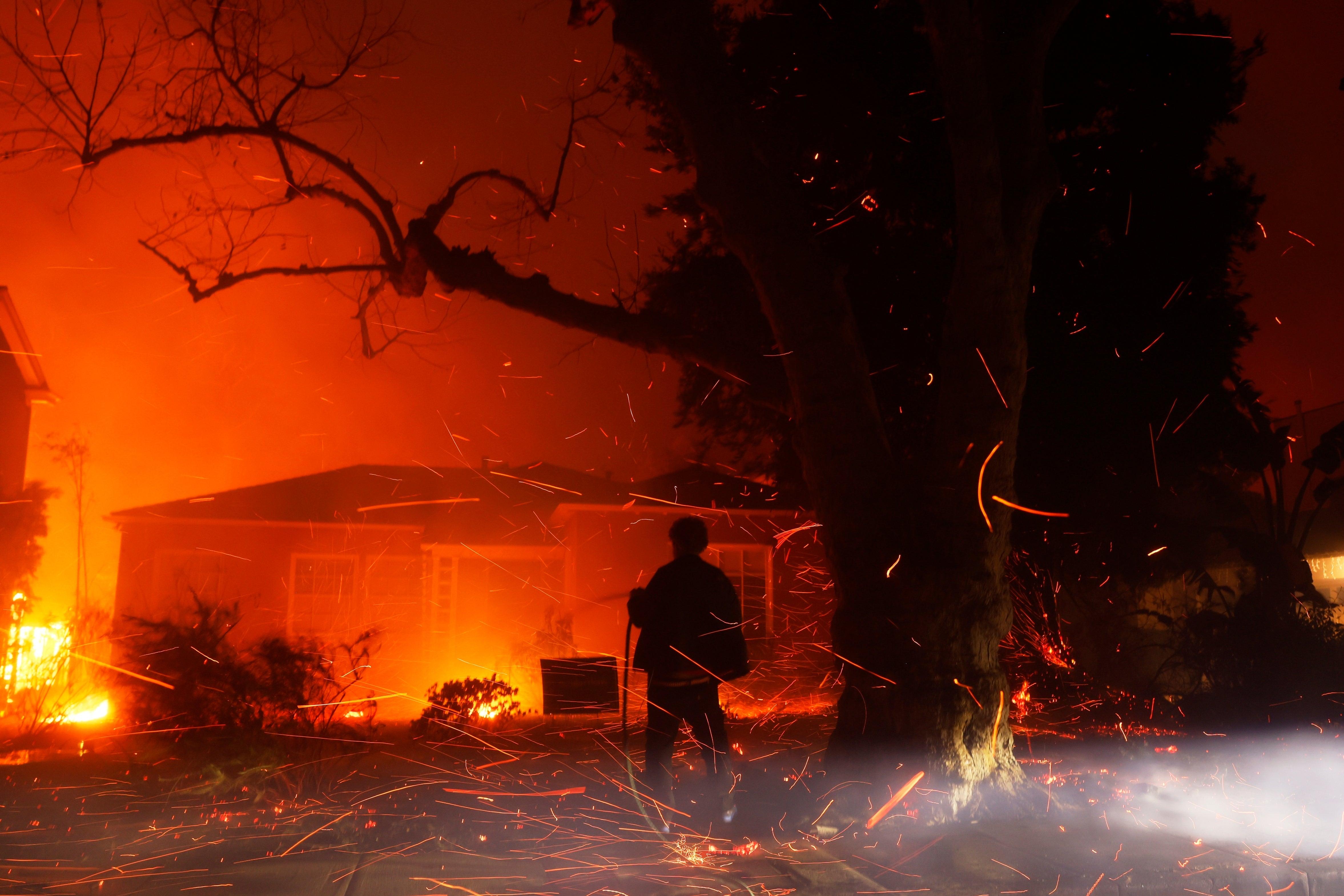 A person tries to hose down embers from the Palisades Fire in the Pacific Palisades neighborhood of Los Angeles