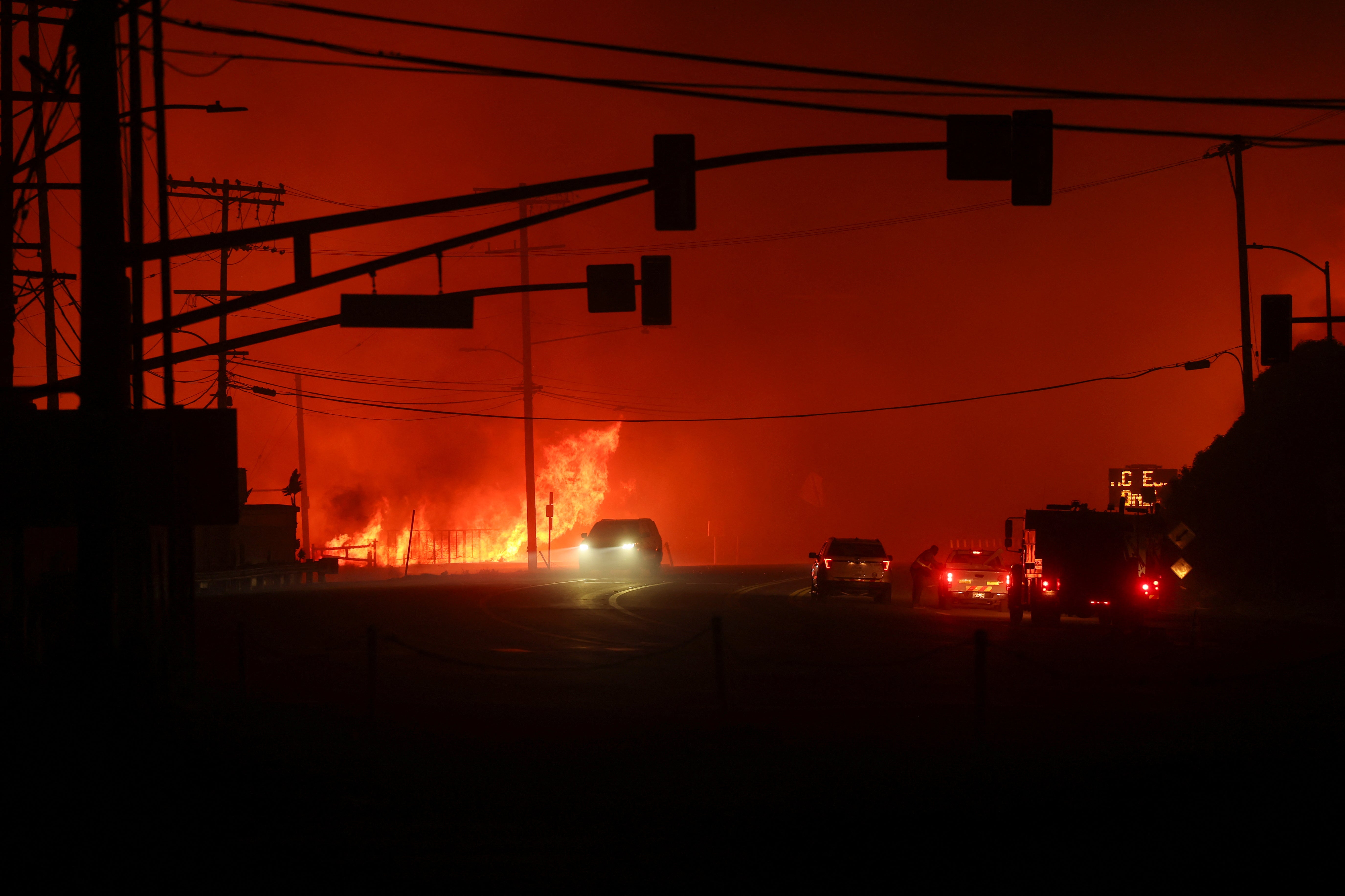 Vehicles drive past flames along the Pacific Coast Highway, as a wildfire burns in the Pacific Palisades neighborhood of west Los Angeles, California