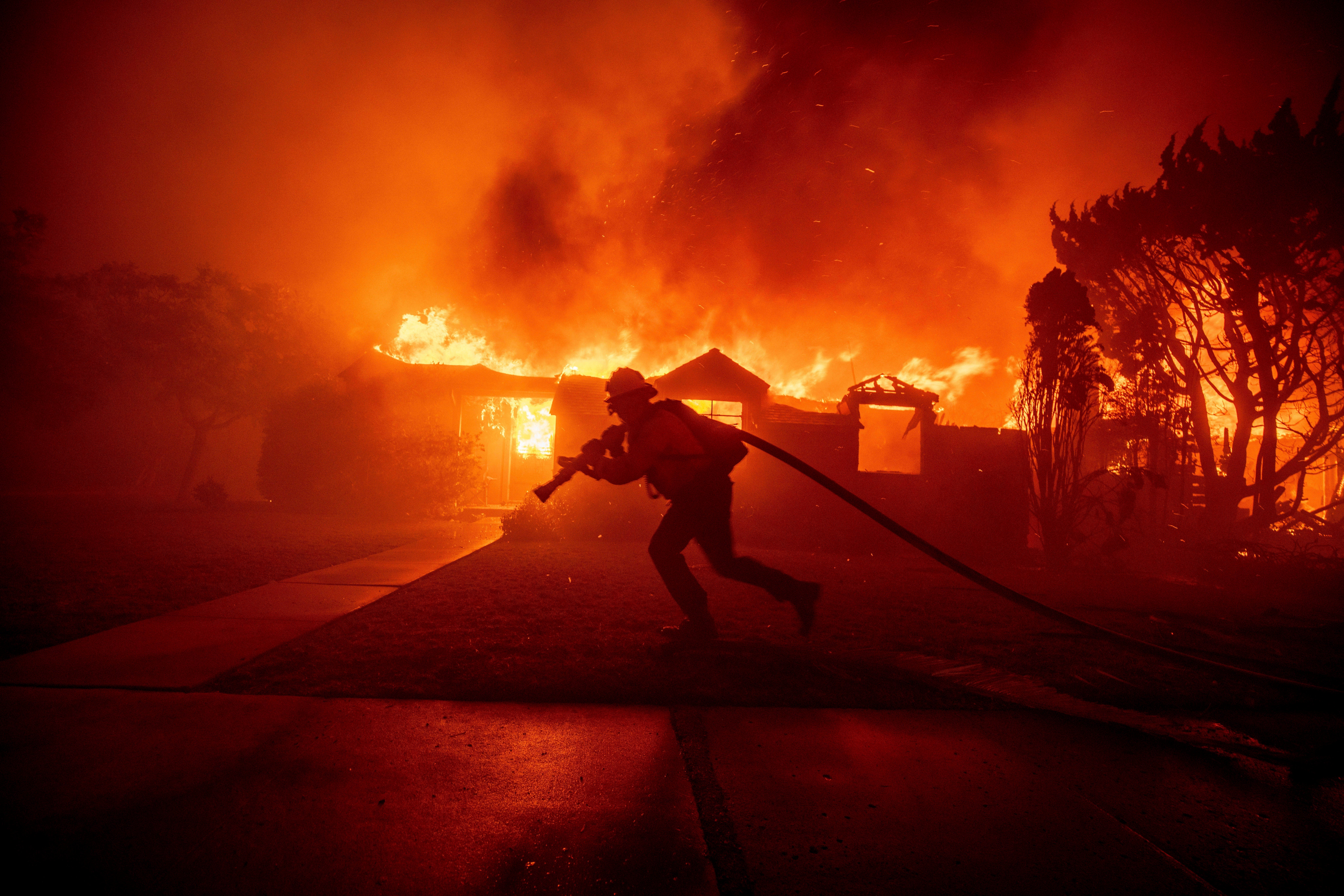 A firefighter battles the Palisades Fire as it burns a structure in the Pacific Palisades neighborhood of Los Angeles, Tuesday