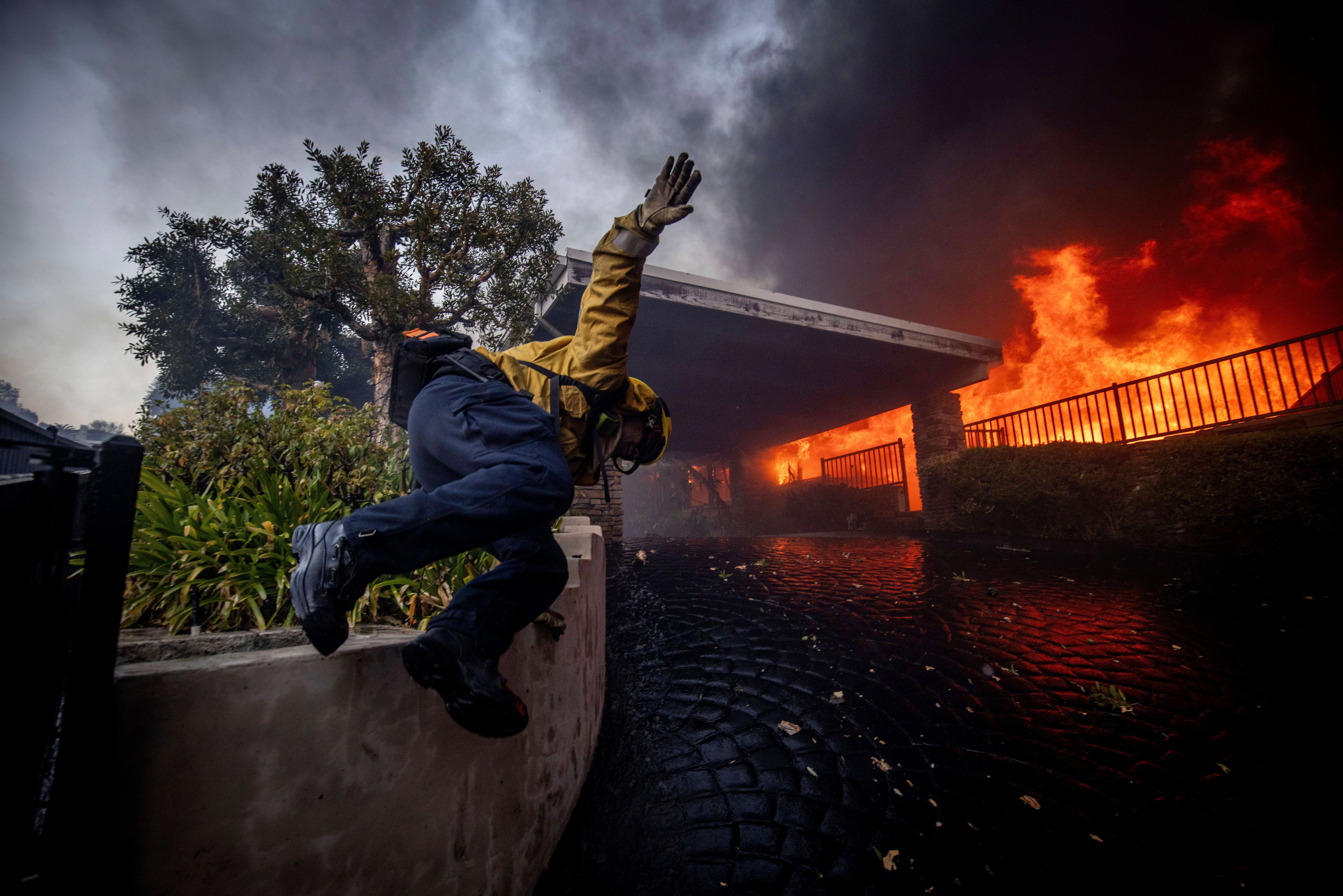 A firefighter jumps over a fence while fighting the Palisades Fire in the Pacific Palisades neighborhood of Los Angeles, Tuesday, 7 January 2025