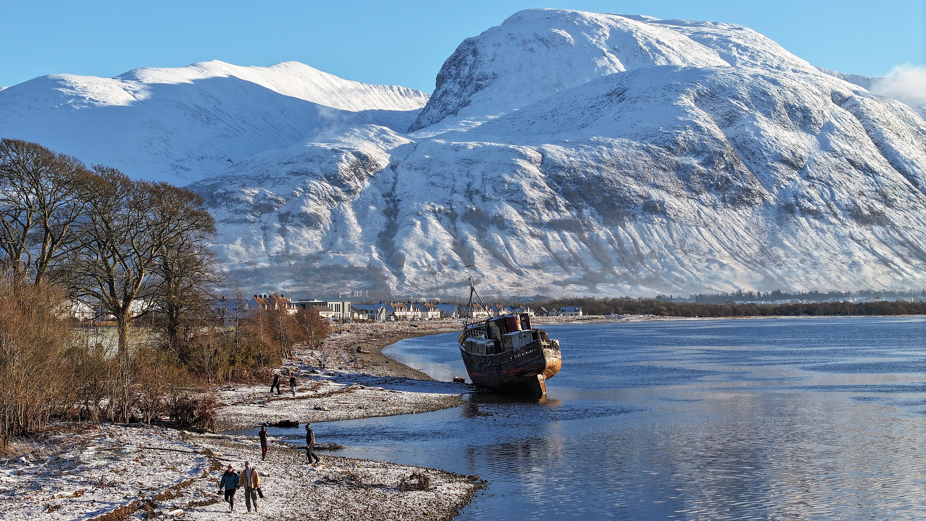 People view a former fishing boat on the shore of Loch Linnhe in front of Ben Nevis