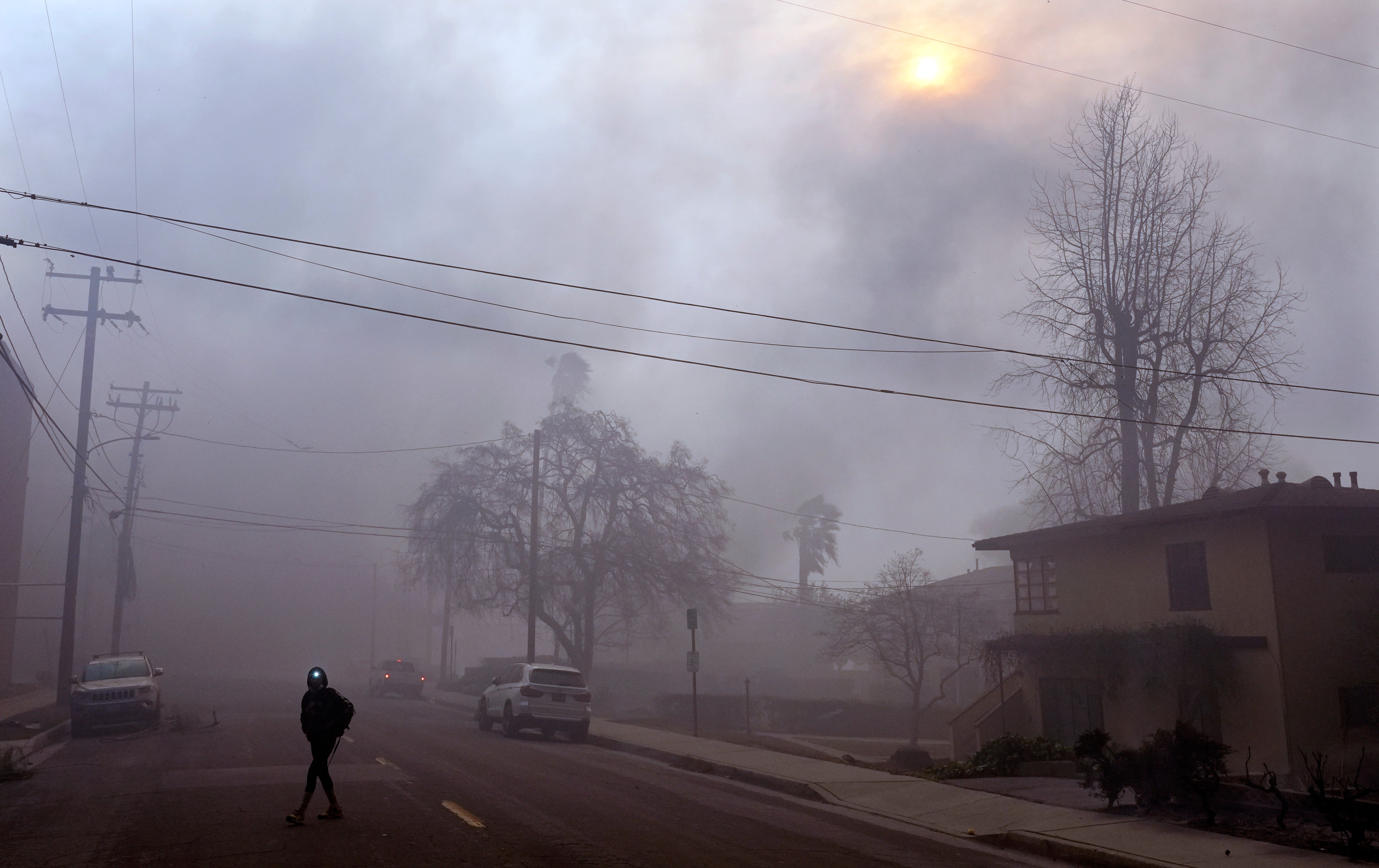 A pedestrian uses a flashlight on a smoke-filled street in Pasadena, California, on Wednesday. Transit there was suspending amid the wildfire threat