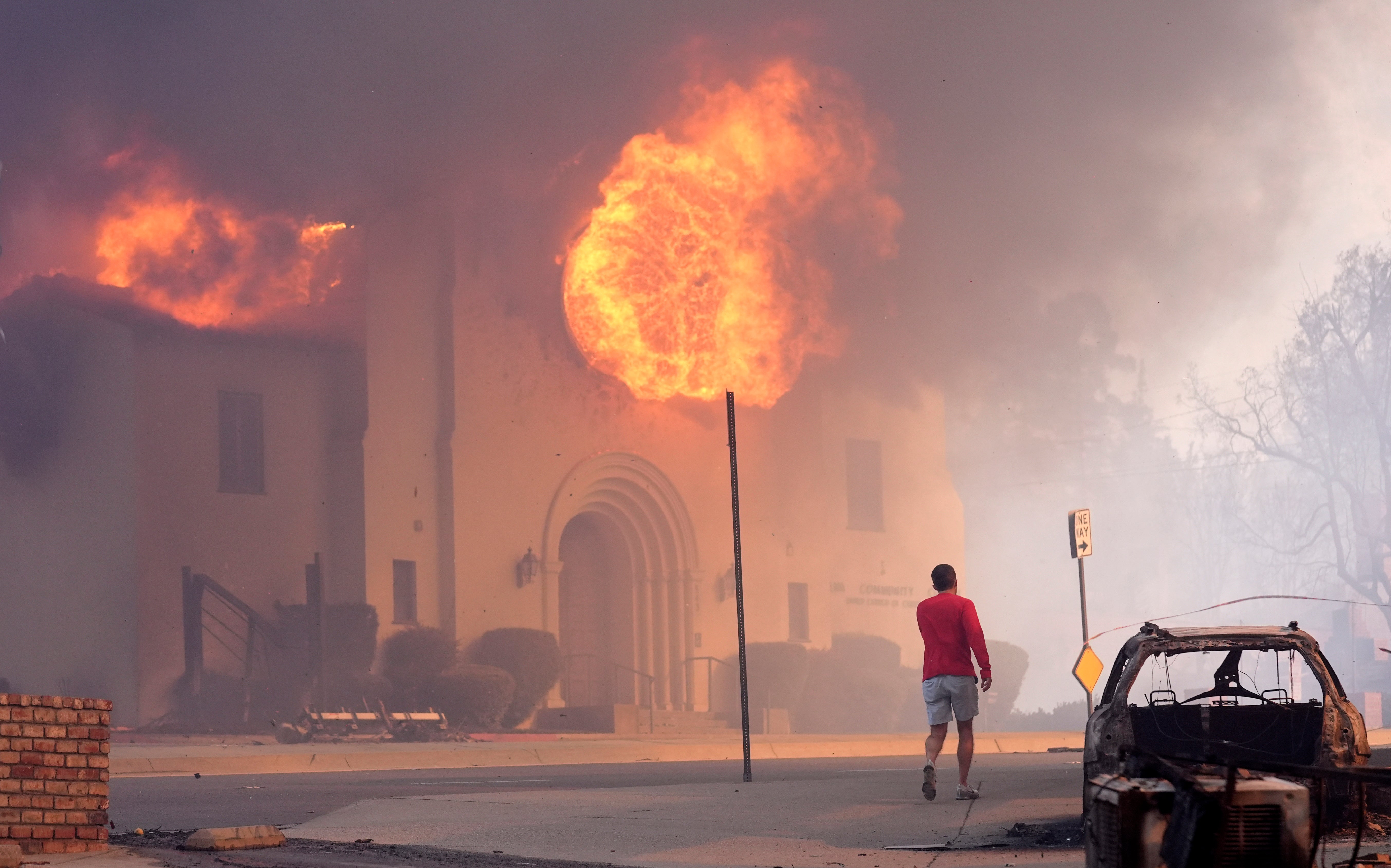 A pedestrian walks across from the burning Altadena Community Church in Pasadena, California, on Wednesday. The city said its public counters would be closed due to wind and fire