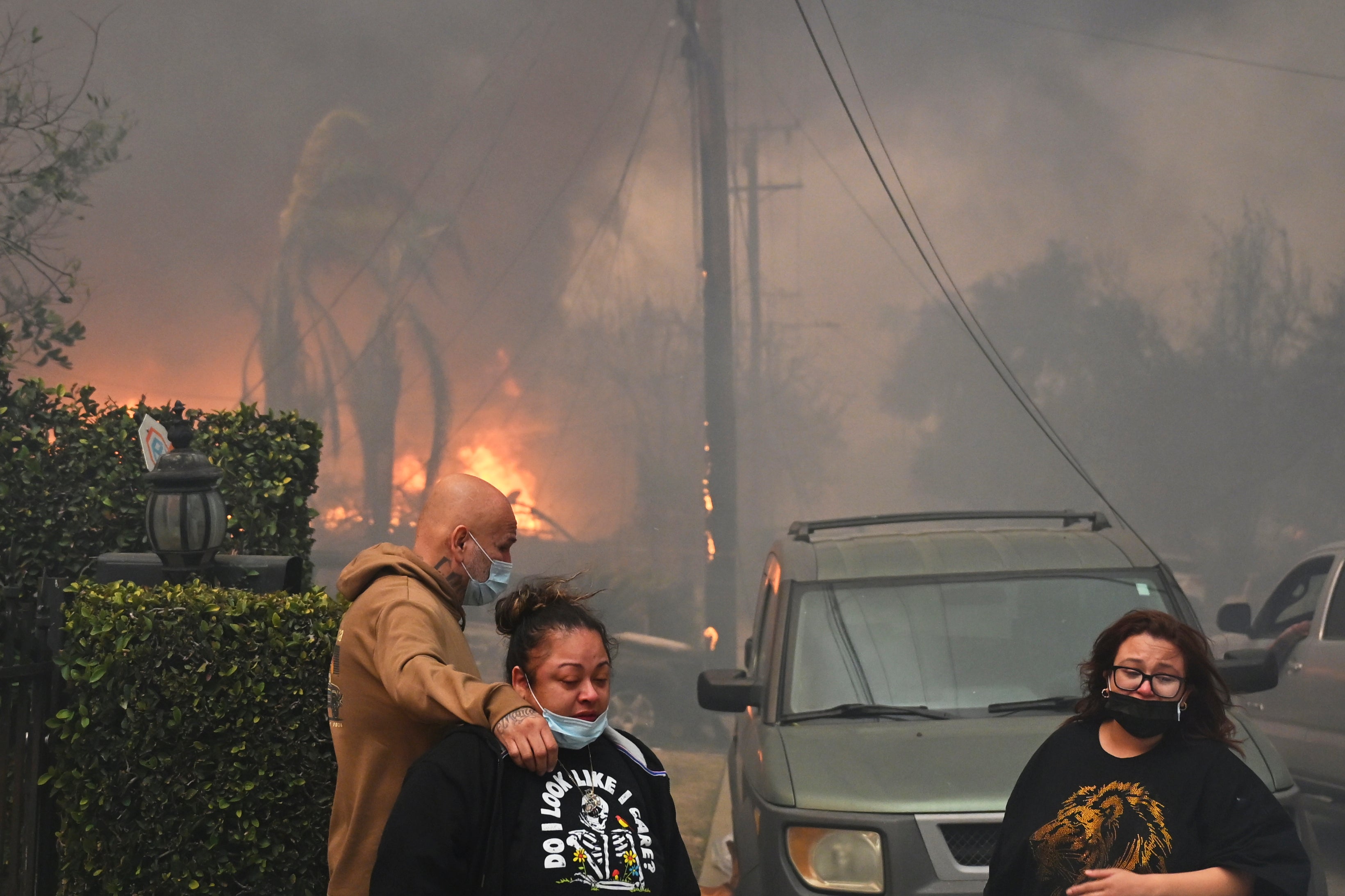 Residents embrace in front of burning structures as the Eaton Fire advances Wednesday Altadena, California. The fire was not contained, officials said