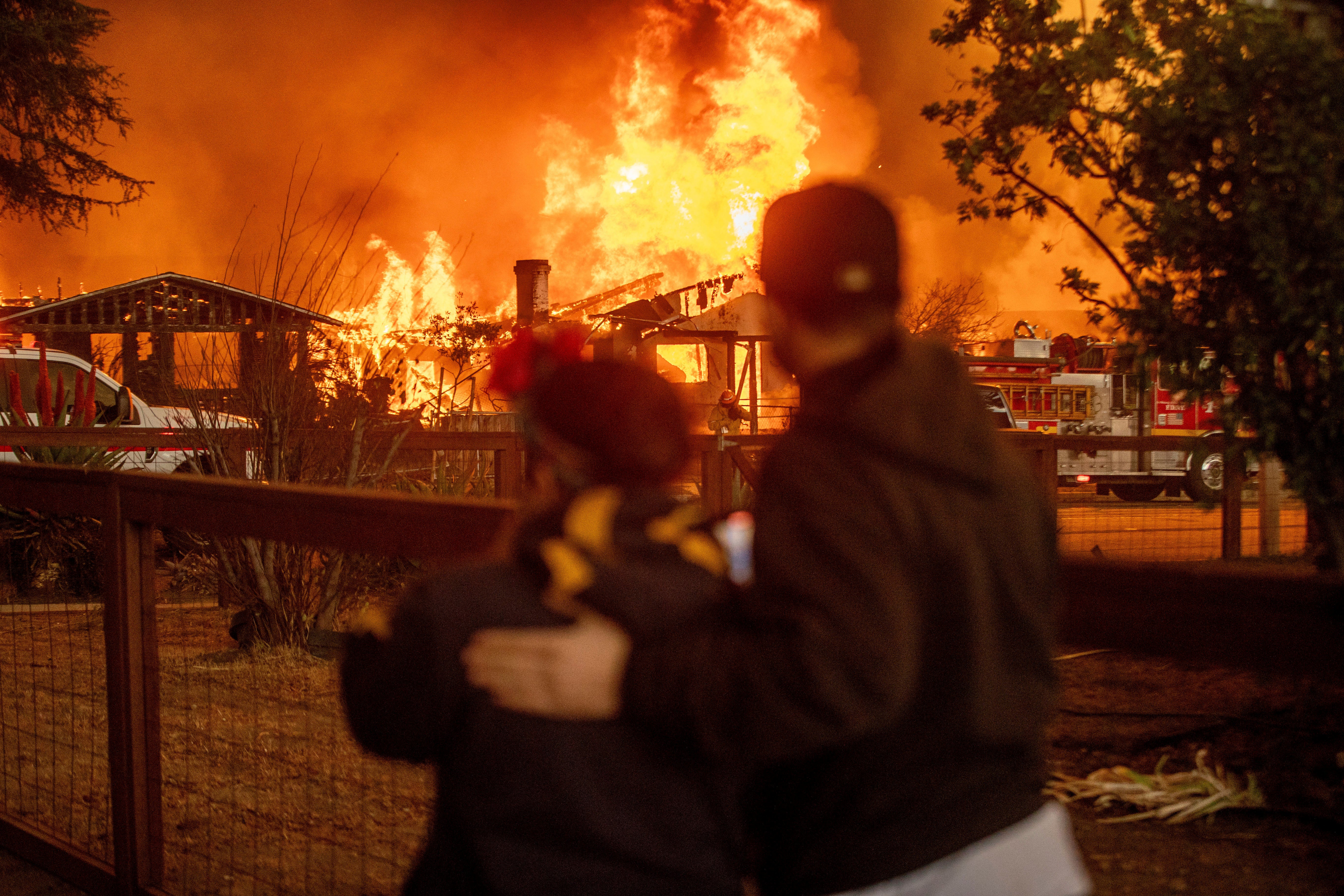 People watch as the Eaton Fire engulfs a structure on Wednesday in Altadena, California. The Eaton Fire was continuing to balloon as strong winds continued