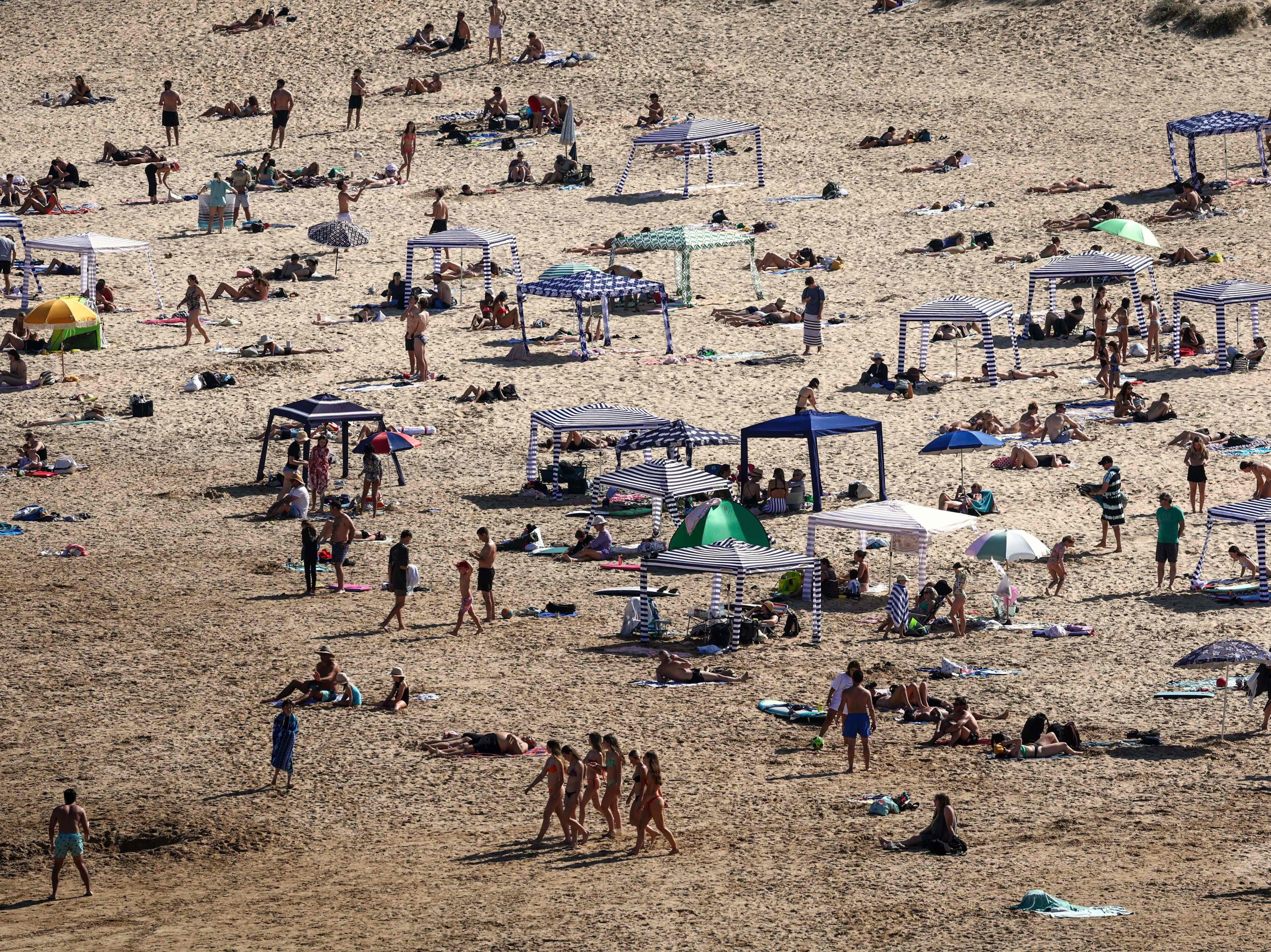 File. Beachgoers sit under make-shift cabanas as others stand on the sand at Freshwater Beach, located in the northern beaches area of Sydney