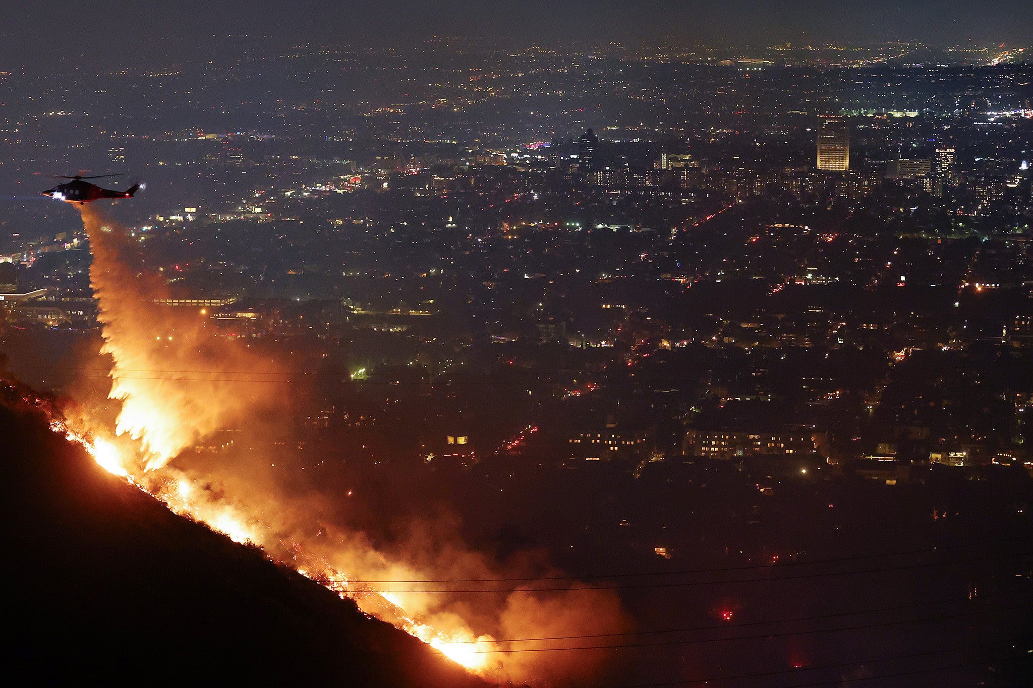 A firefighting helicopter drops water as the Sunset Fire burns in the Hollywood Hills on Wednesday evening